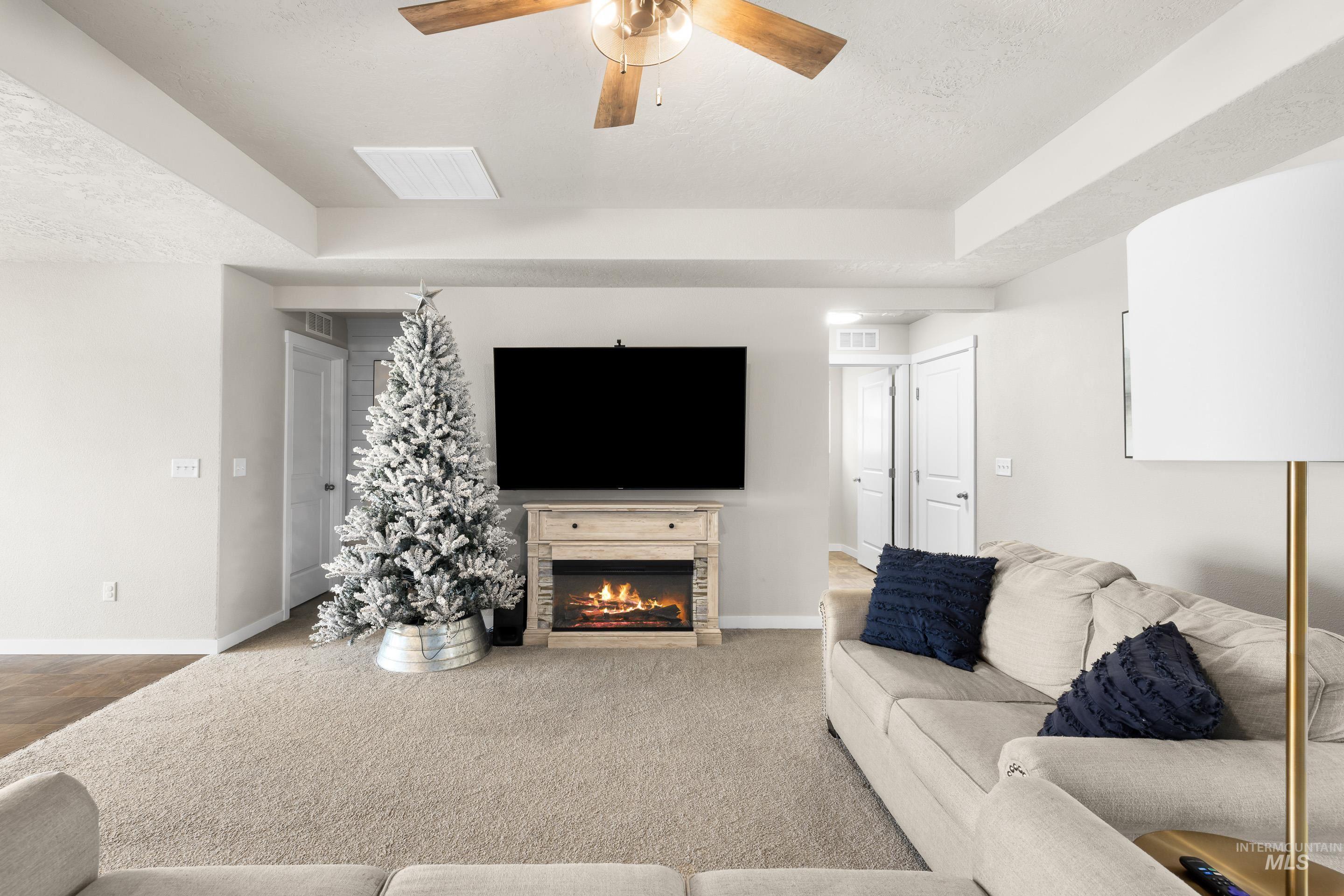Carpeted living room featuring a lit fireplace, a ceiling fan, and a textured ceiling