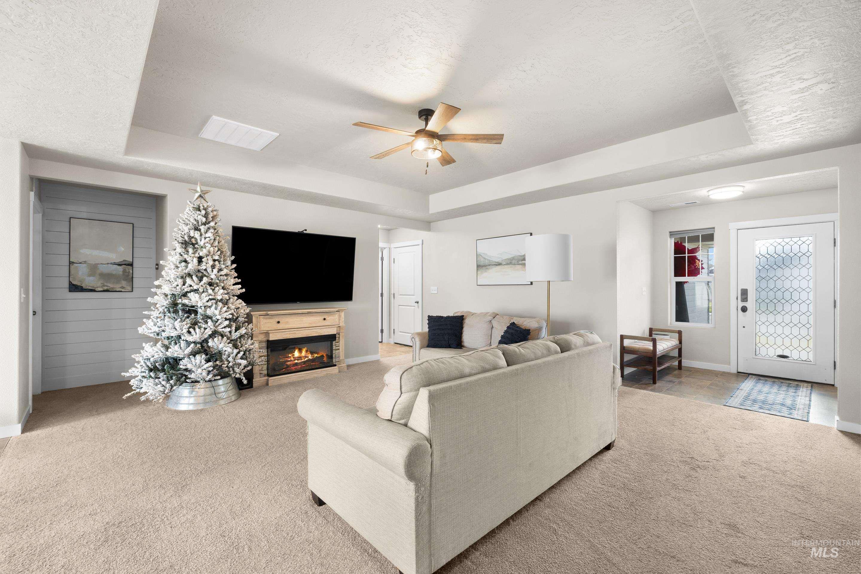 Carpeted living area with a tray ceiling, a textured ceiling, a glass covered fireplace, and a ceiling fan