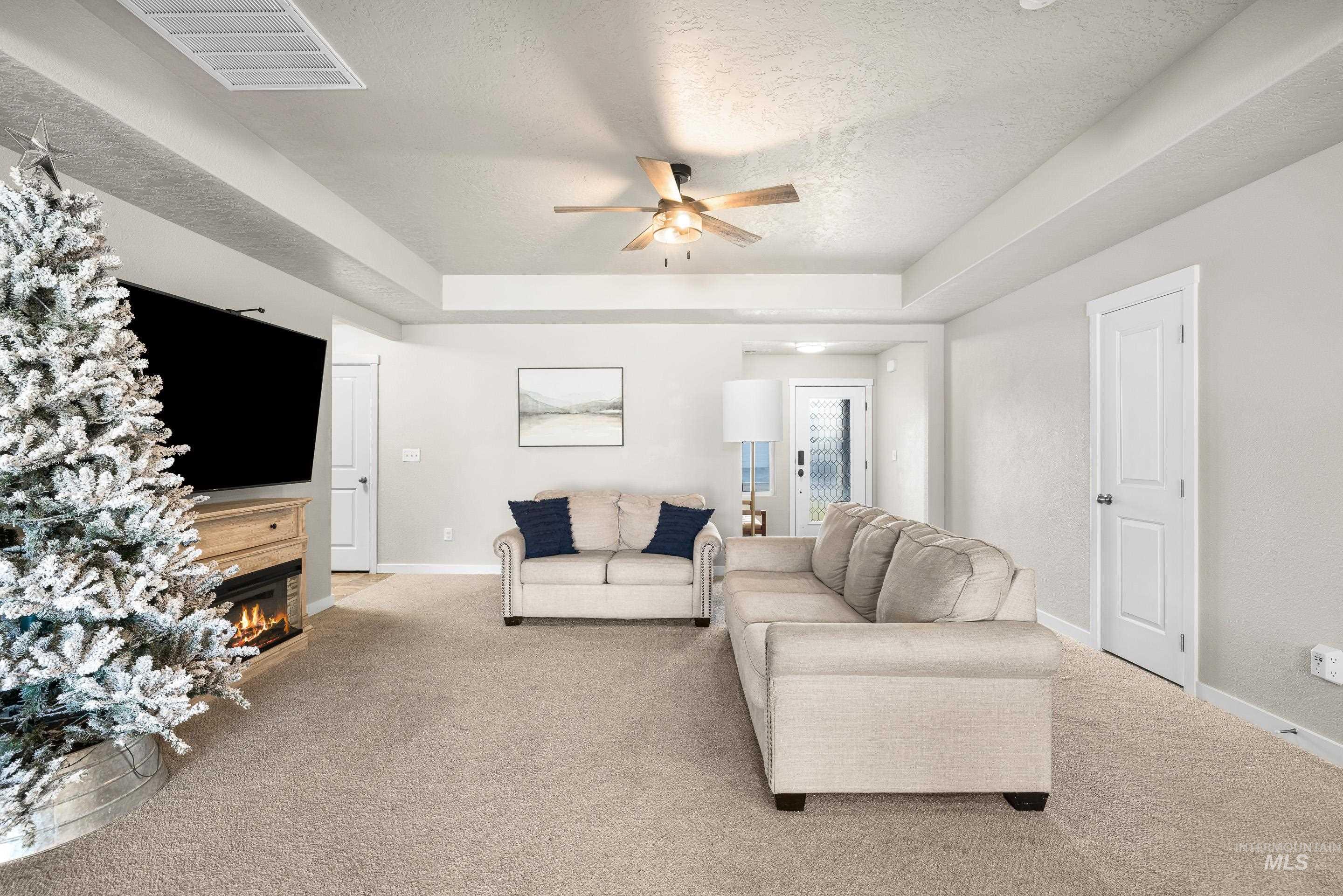 Living area with carpet, a textured ceiling, a warm lit fireplace, a ceiling fan, and a tray ceiling