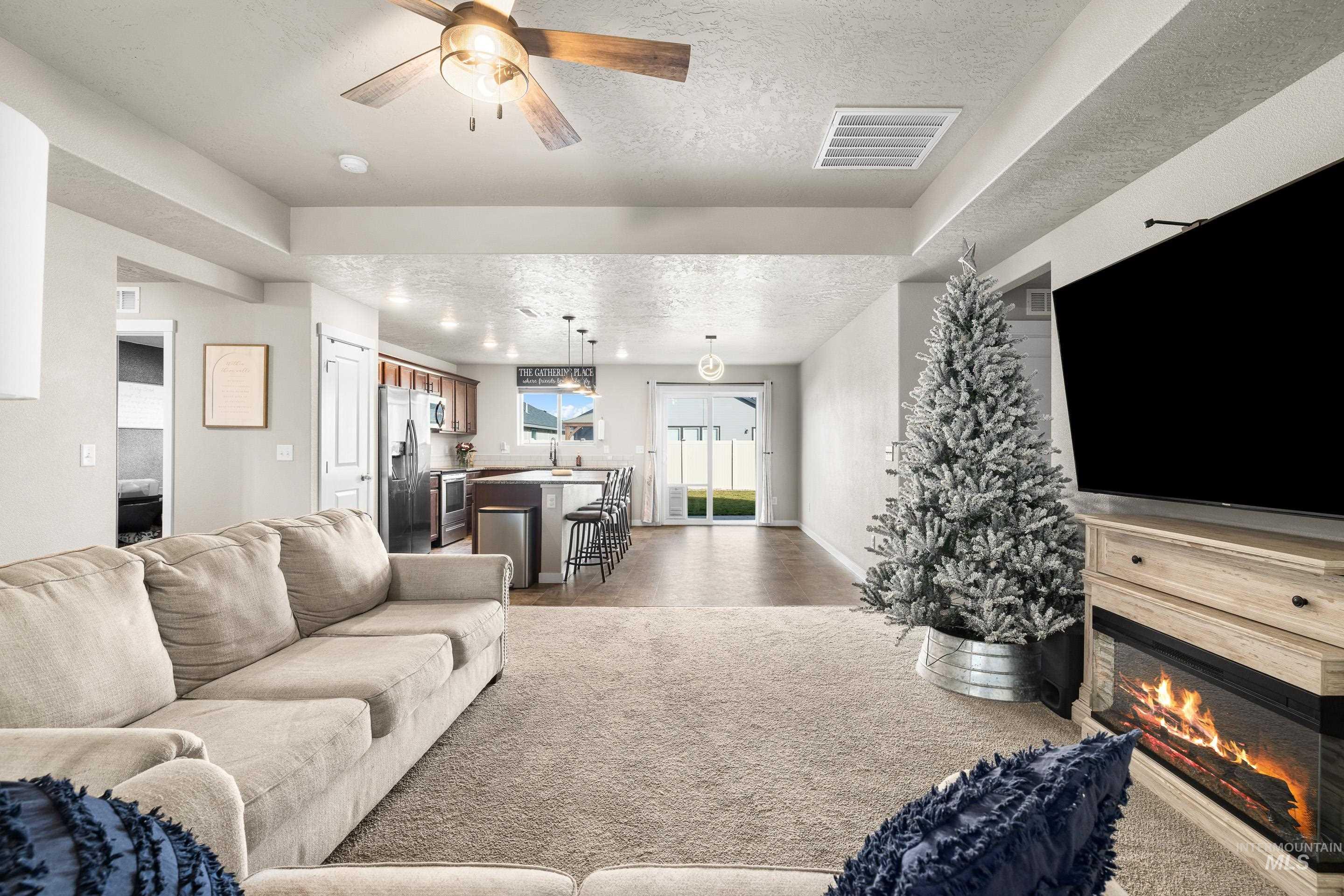 Living area featuring a textured ceiling, a ceiling fan, and a glass covered fireplace