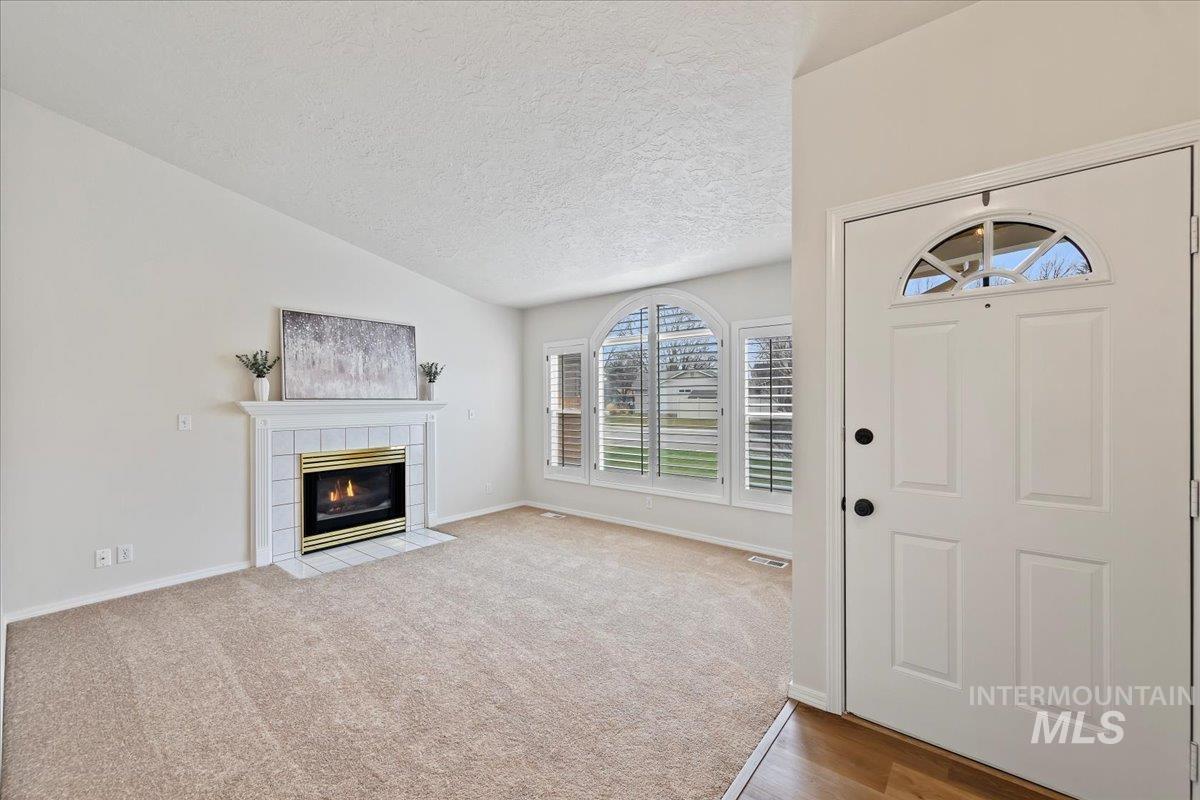 Entrance foyer leads to front living room featuring a tiled gas log fireplace with wood mantel, a lofted ceiling, BRAND NEW carpet & pad, Picture window with Plantation Shutters!