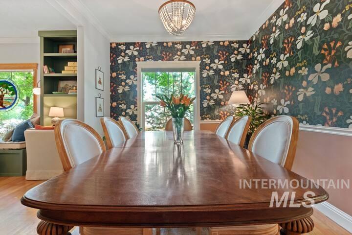 Dining space with wallpapered walls, wood finished floors, healthy amount of natural light, a chandelier, and ornamental molding