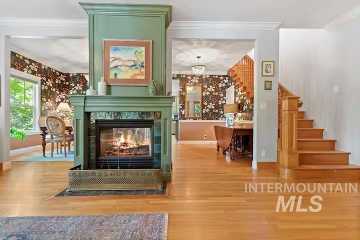 Detailed view of wood finished floors, crown molding, a multi sided fireplace, and a chandelier