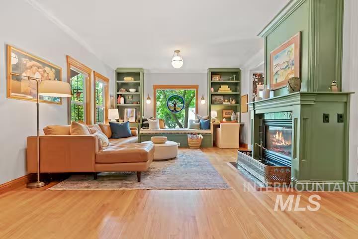 Living room with built in features, a glass covered fireplace, and light wood-style flooring