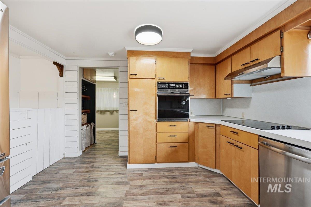Kitchen featuring black appliances, light countertops, light wood-style floors, under cabinet range hood, and ornamental molding