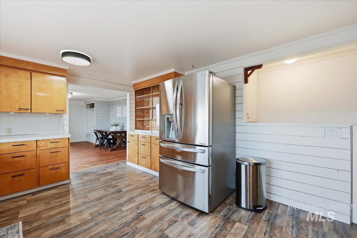 Kitchen with stainless steel refrigerator with ice dispenser, light countertops, dark wood-style flooring, ornamental molding, and brown cabinets