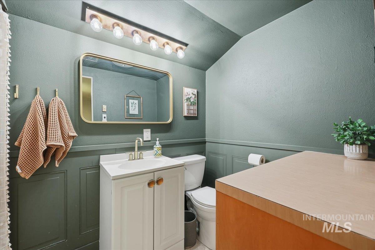 Bathroom featuring vanity, wainscoting, a textured wall, vaulted ceiling, and a decorative wall