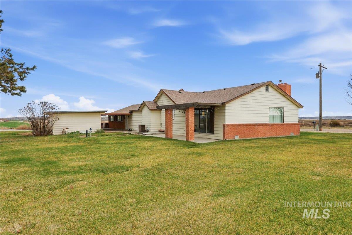 Back of house with brick siding, a lawn, a chimney, and a patio area