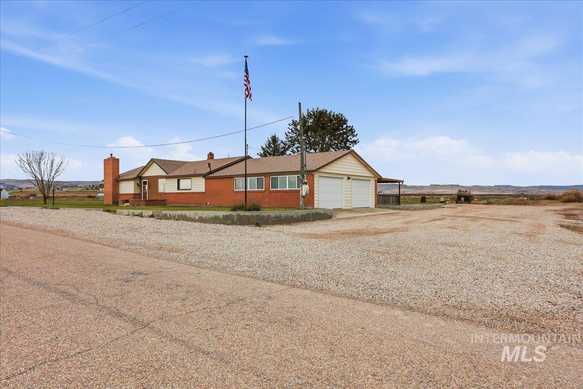 View of front of house featuring gravel driveway, a chimney, brick siding, and a garage