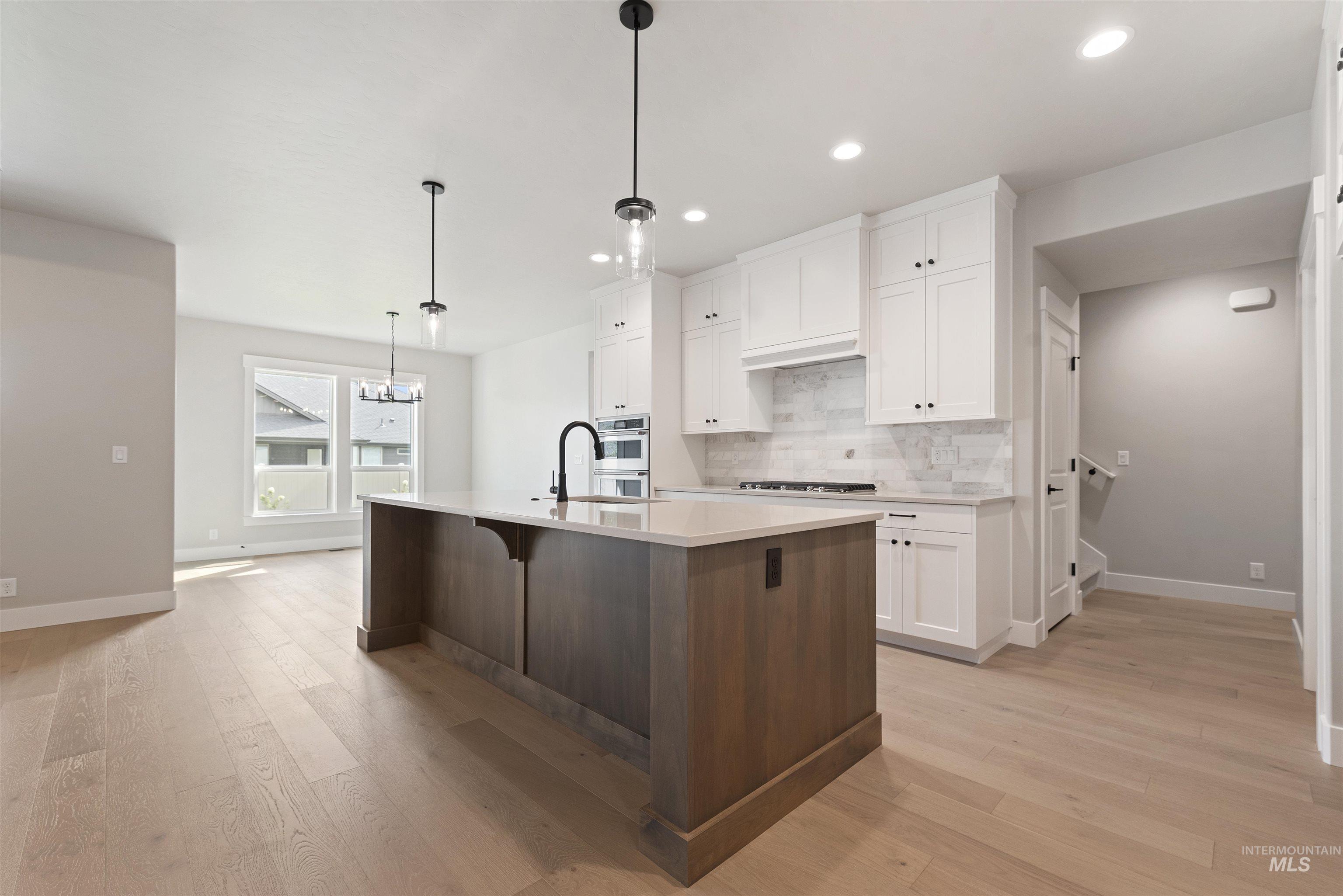 Kitchen with white cabinets, hanging light fixtures, a kitchen island with sink, backsplash, and a kitchen breakfast bar