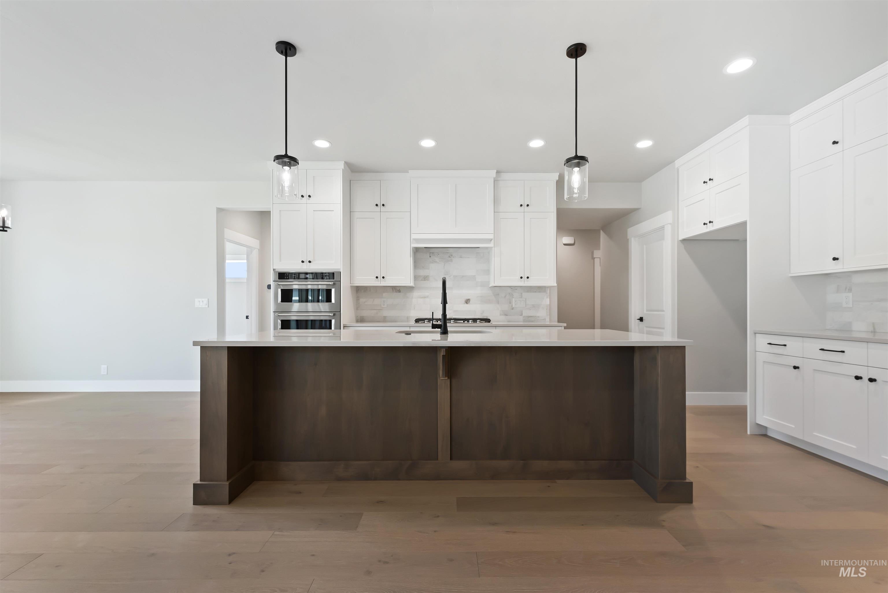 Kitchen featuring white cabinets, hanging light fixtures, a kitchen island with sink, tasteful backsplash, and recessed lighting