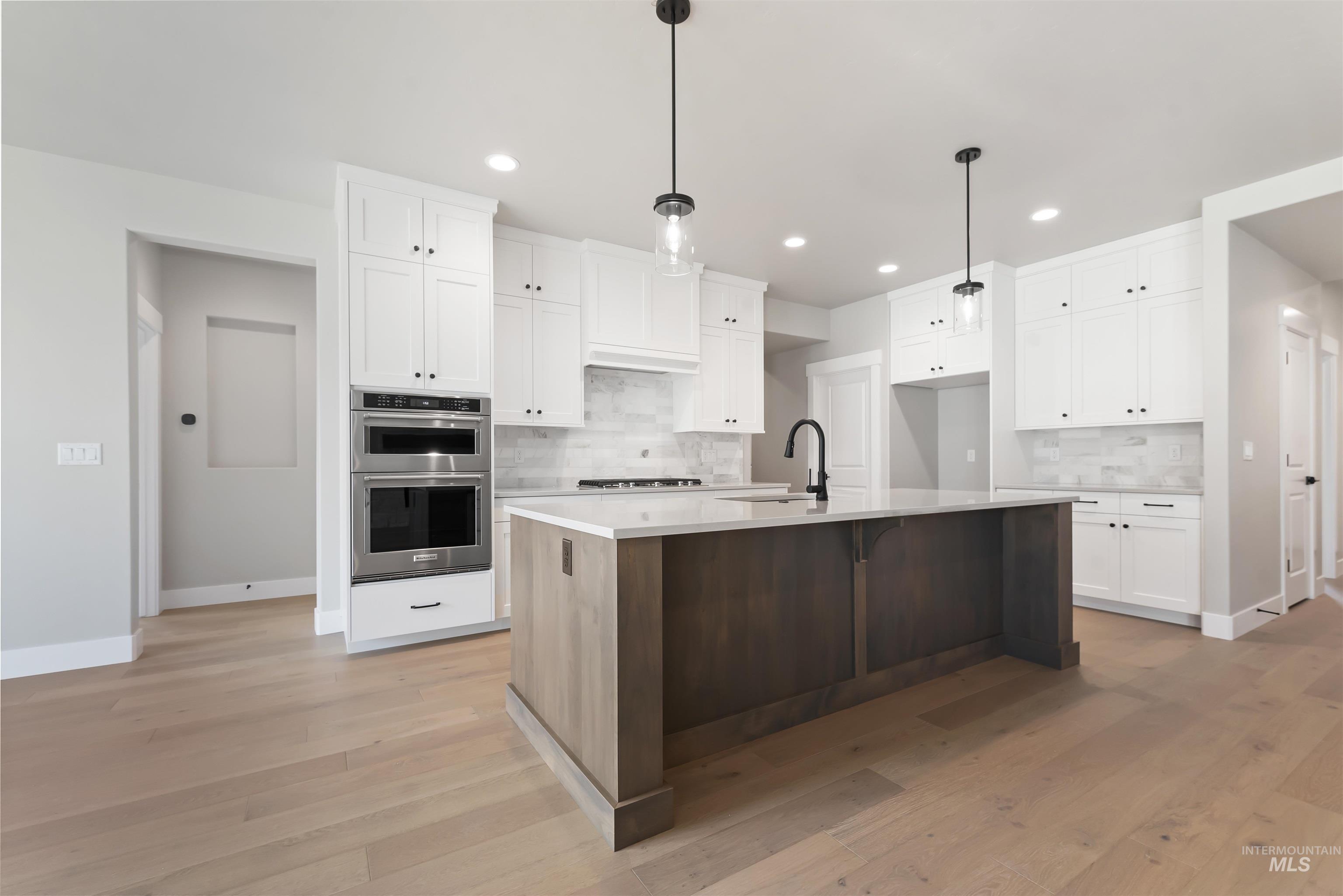 Kitchen featuring white cabinetry, a center island with sink, hanging light fixtures, stainless steel appliances, and decorative backsplash
