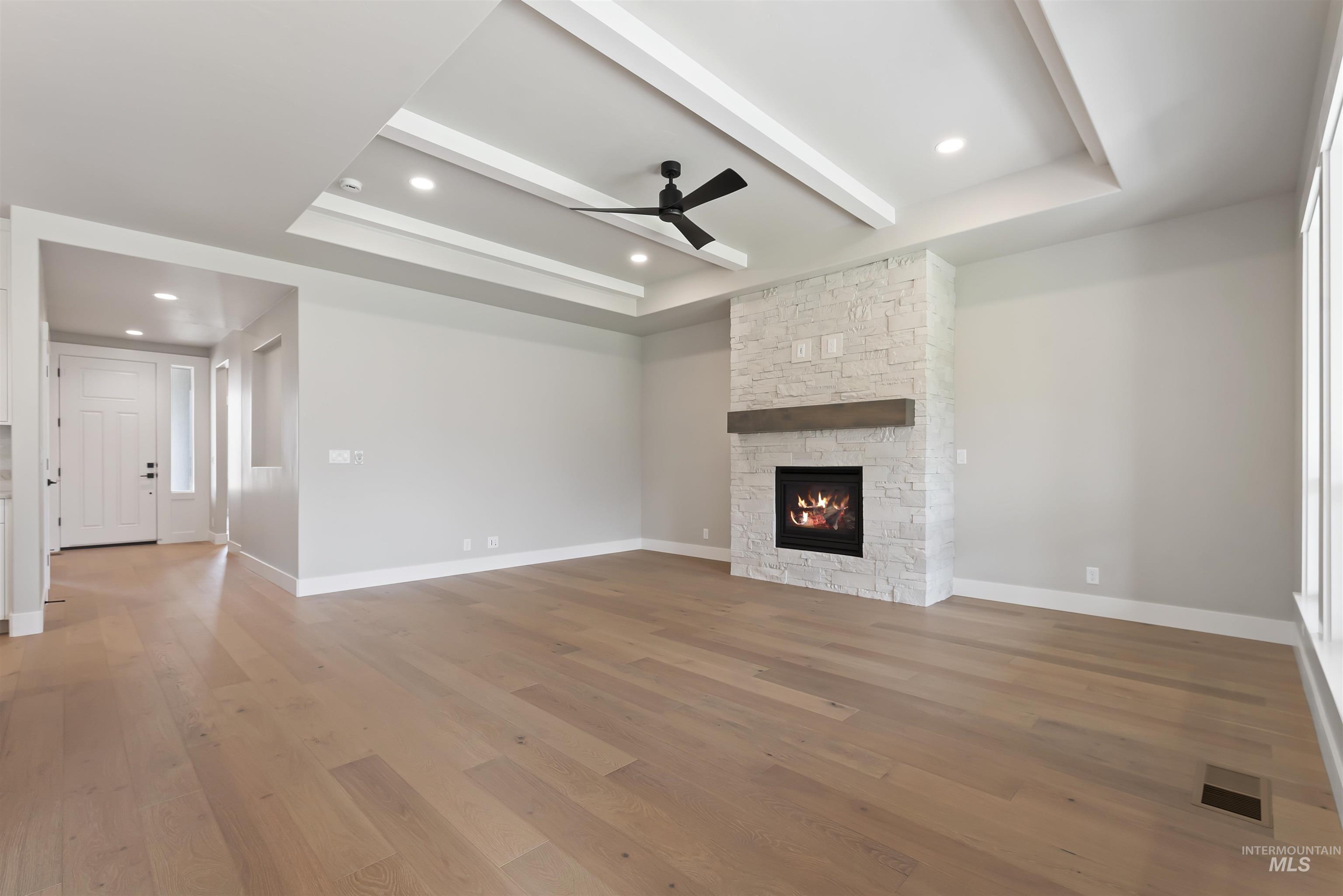 Unfurnished living room featuring ceiling fan, light wood-style flooring, a fireplace, a raised ceiling, and recessed lighting