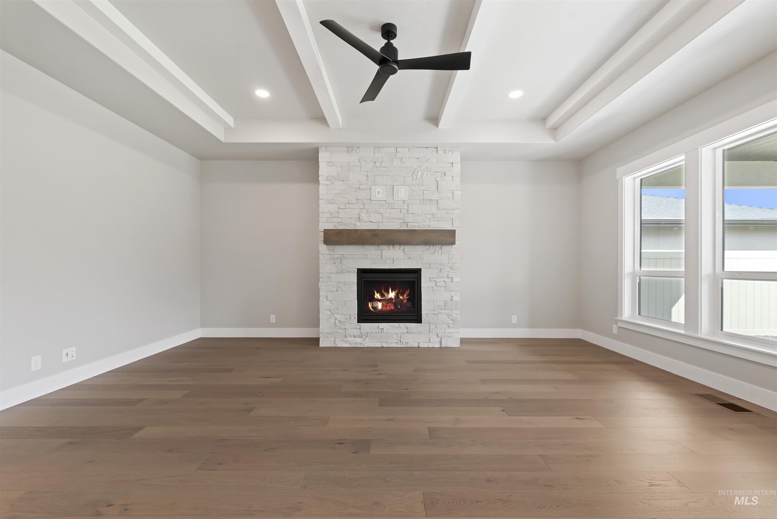 Unfurnished living room with a stone fireplace, dark wood-type flooring, ceiling fan, recessed lighting, and beam ceiling