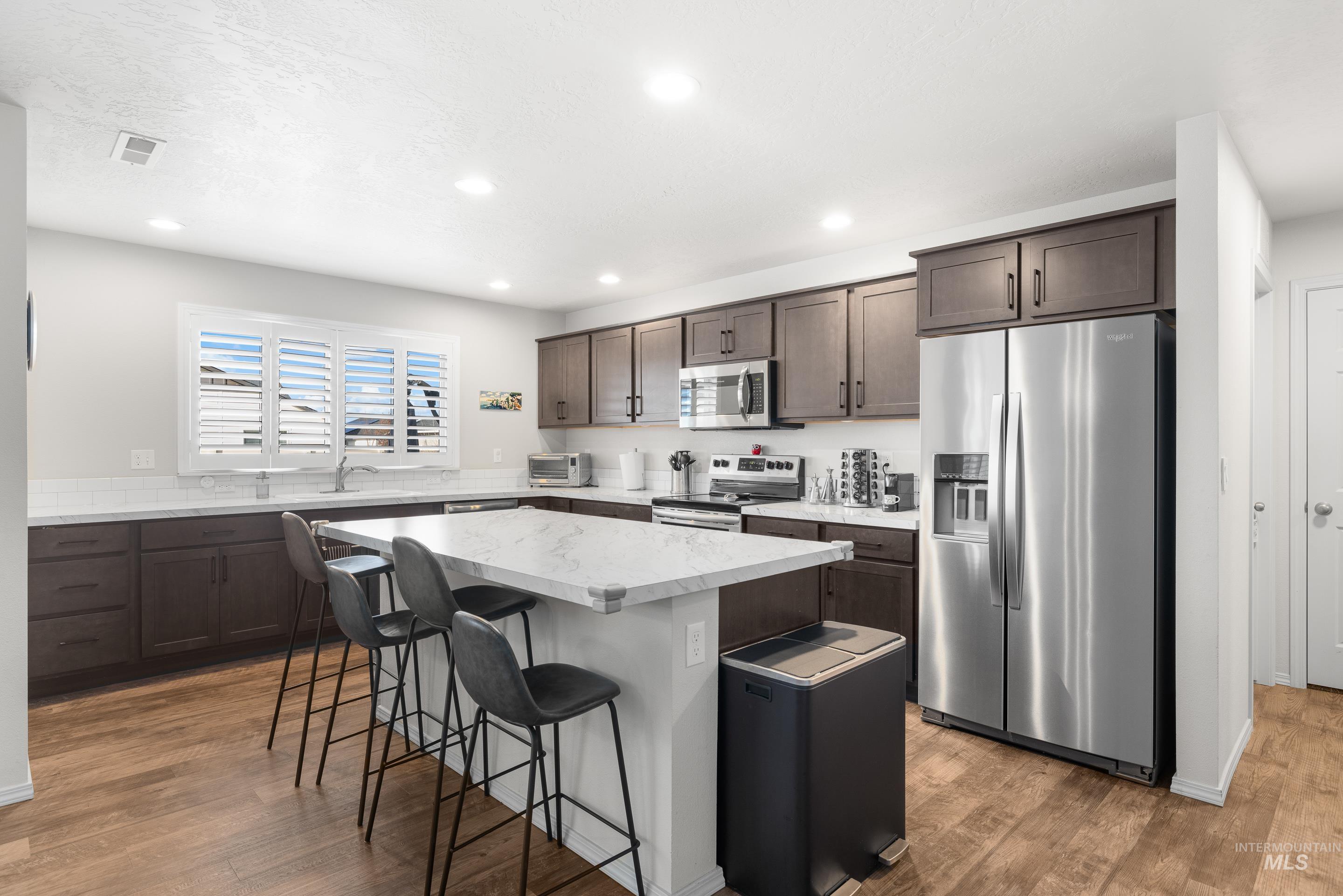 Kitchen with stainless steel appliances, a kitchen breakfast bar, dark brown cabinetry, a kitchen island, and light wood-style floors