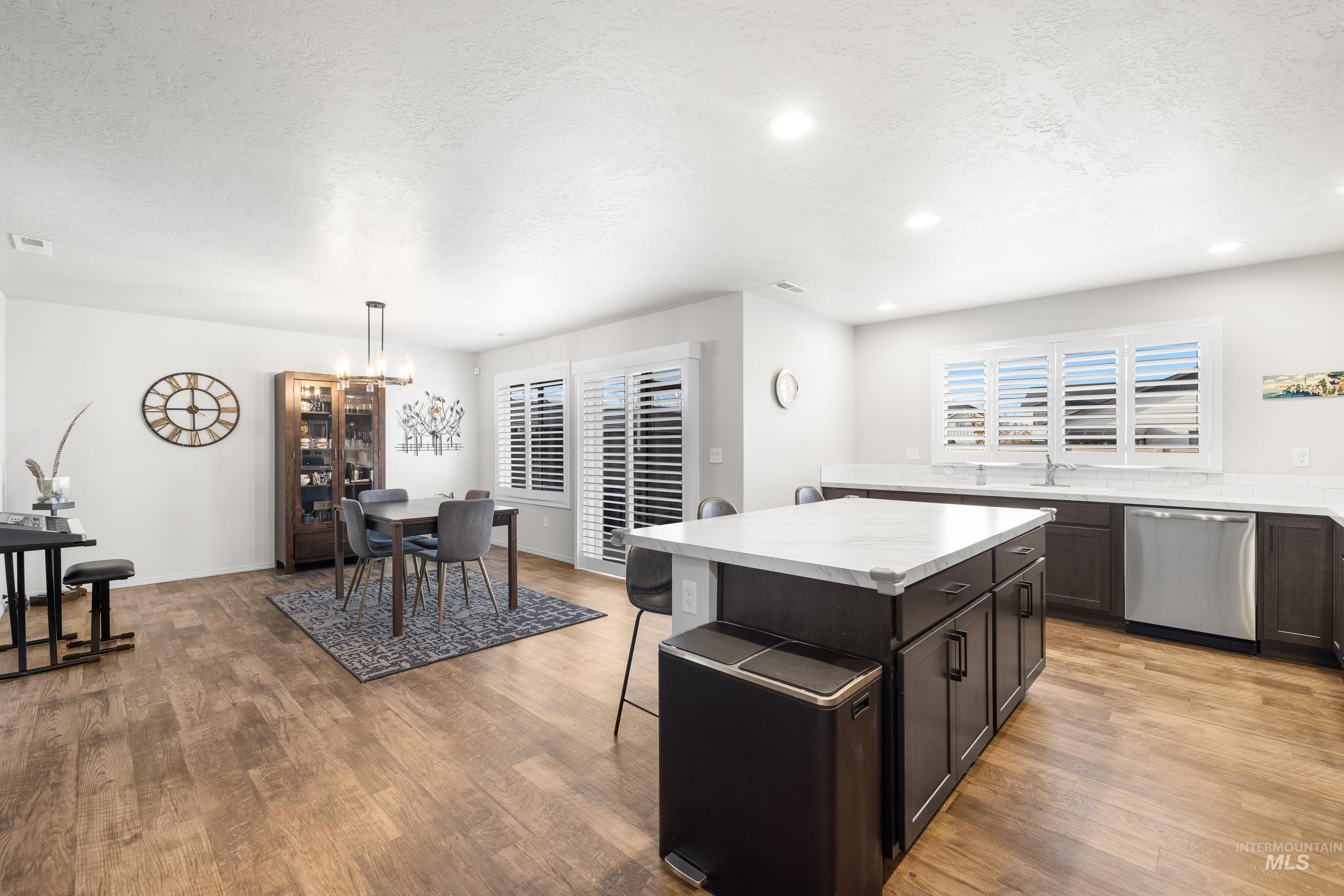 Kitchen featuring a textured ceiling, stainless steel dishwasher, pendant lighting, a breakfast bar, and light wood-type flooring