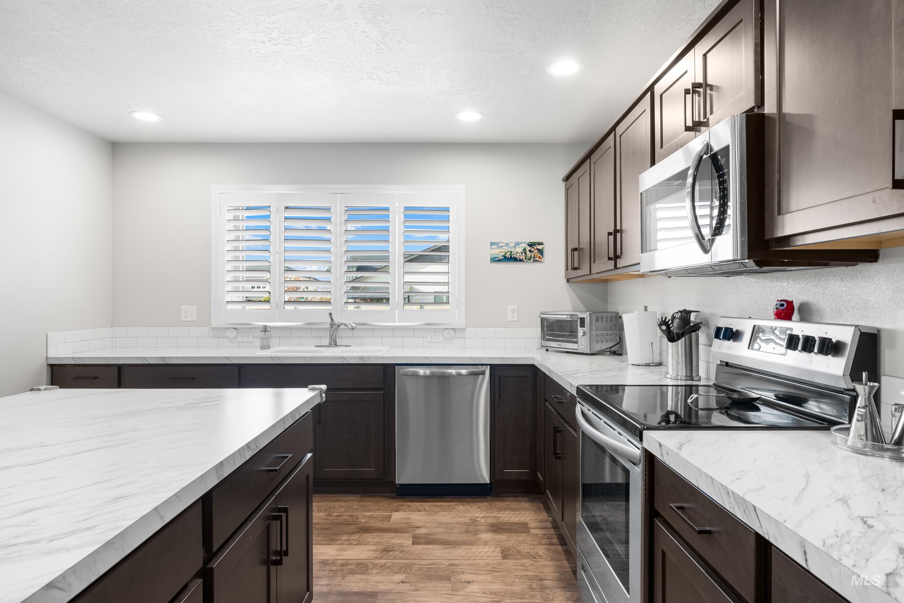 Kitchen with appliances with stainless steel finishes, light countertops, dark brown cabinetry, light wood finished floors, and recessed lighting