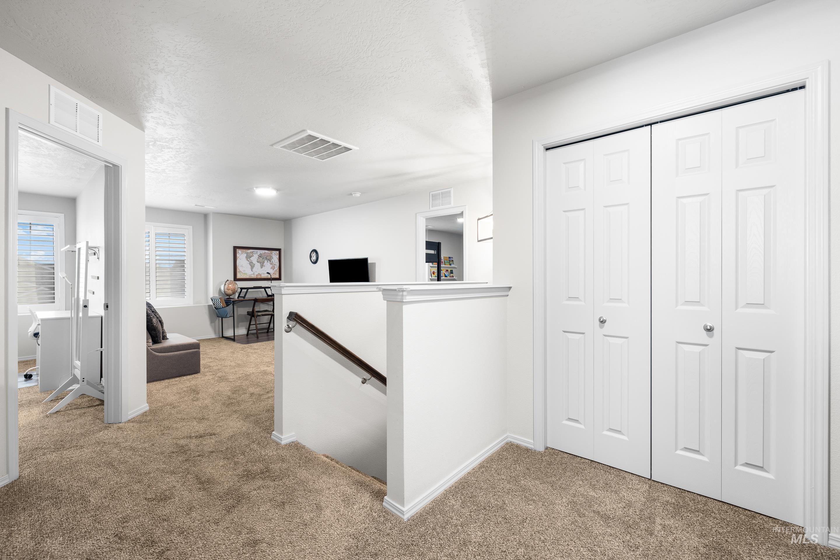 Hall featuring an upstairs landing, light carpet, and a textured ceiling
