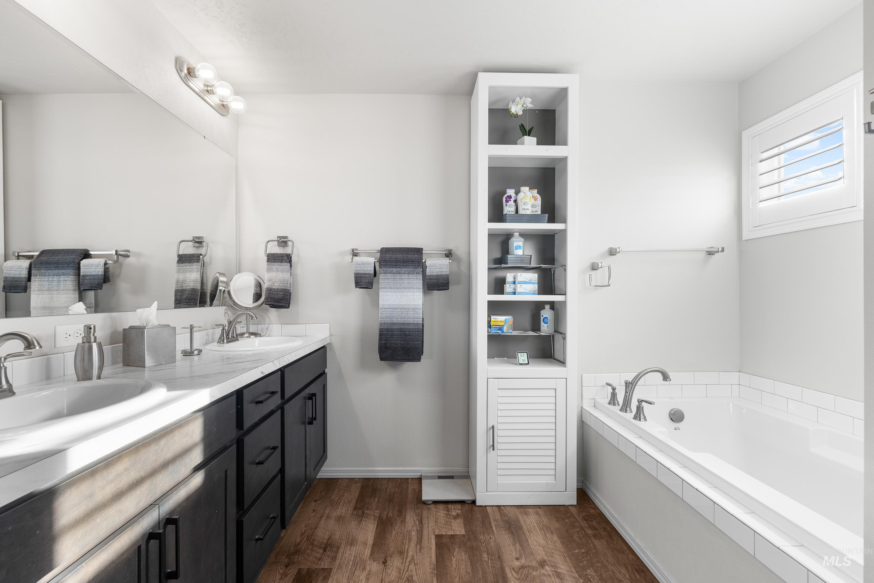 Full bathroom featuring double vanity, a garden tub, and dark wood-type flooring