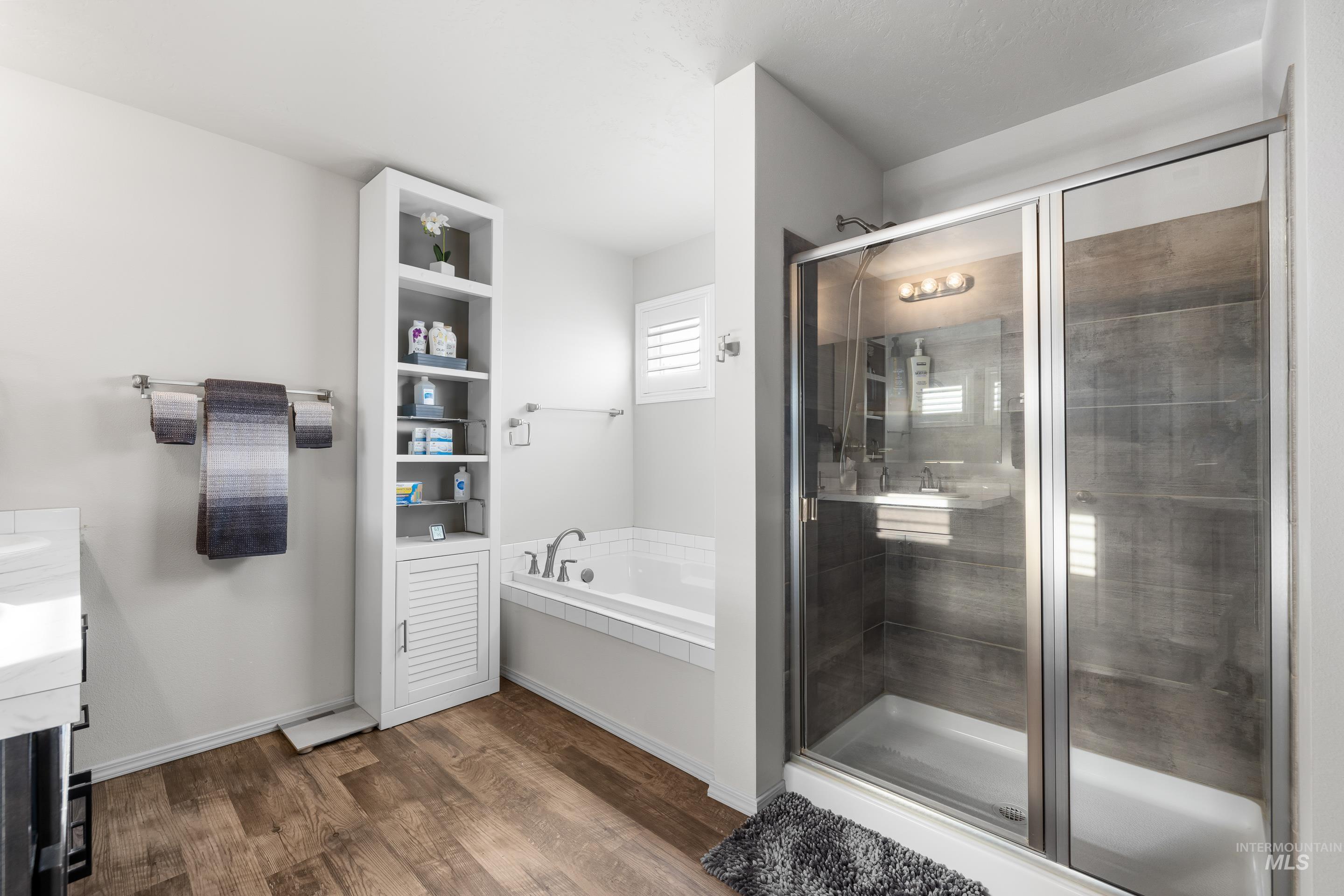 Bathroom featuring vanity, a garden tub, a stall shower, and dark wood-type flooring