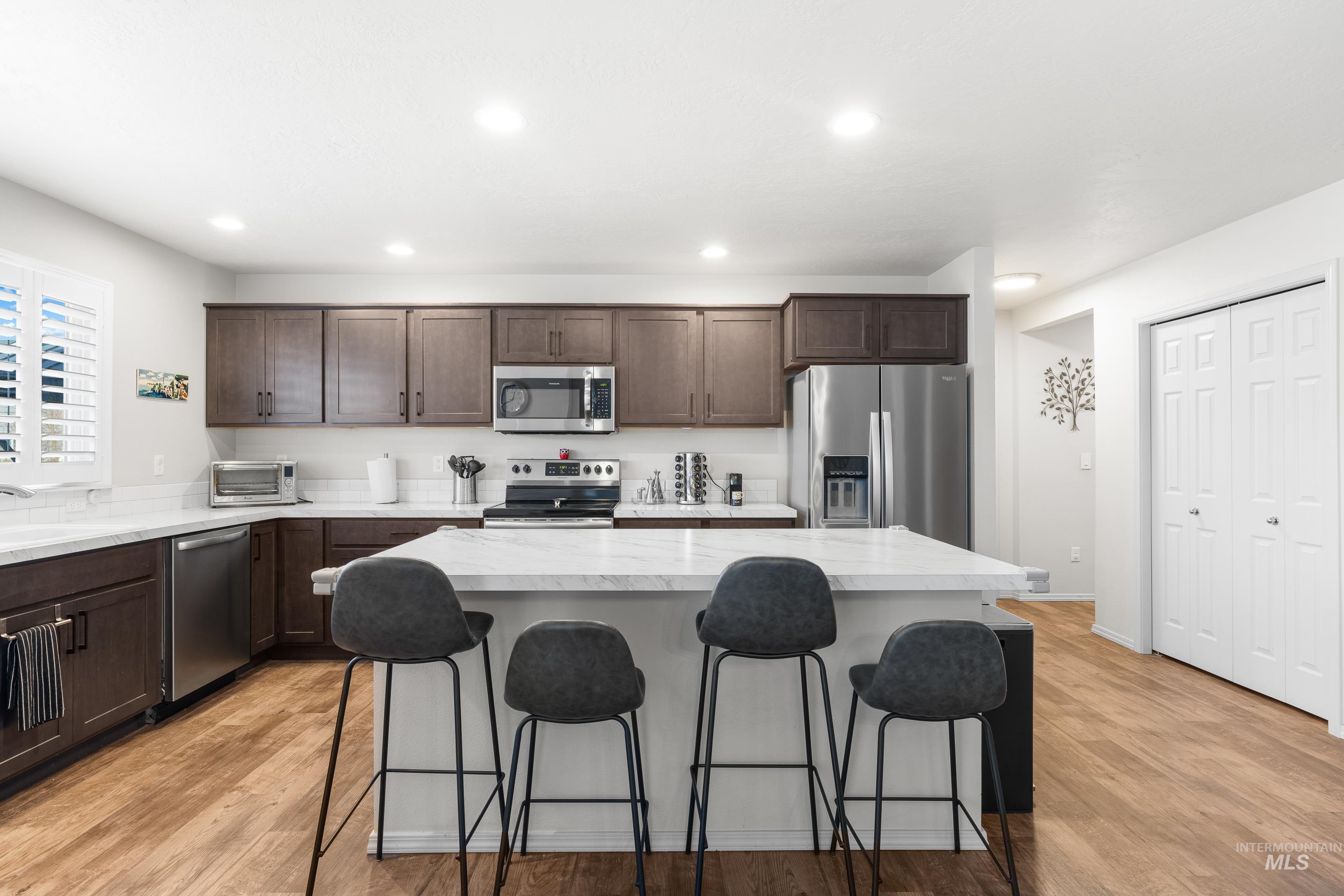 Kitchen with dark brown cabinetry, light countertops, appliances with stainless steel finishes, a breakfast bar area, and a kitchen island