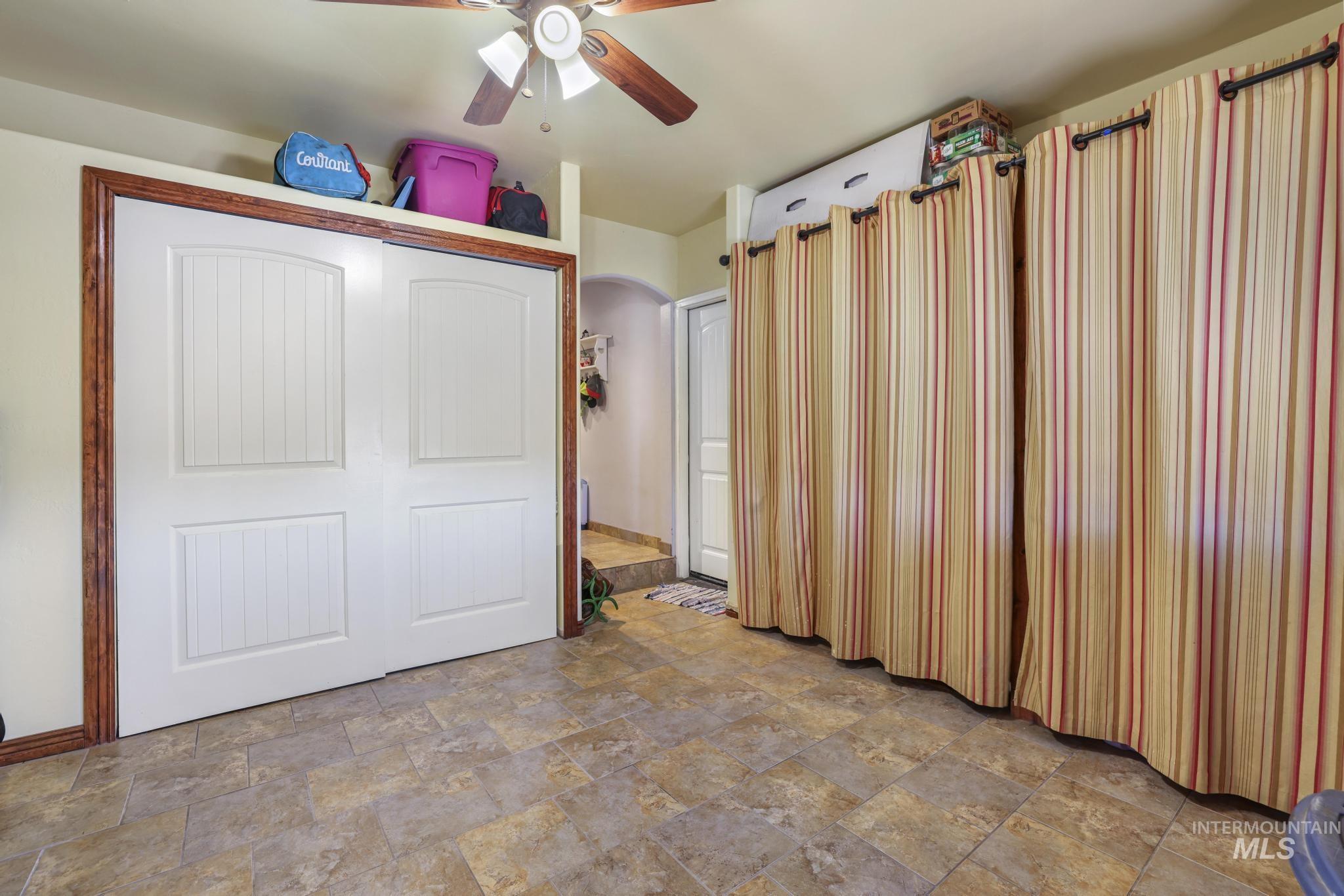 Unfurnished bedroom with stone finish flooring, a closet, a ceiling fan, and arched walkways
