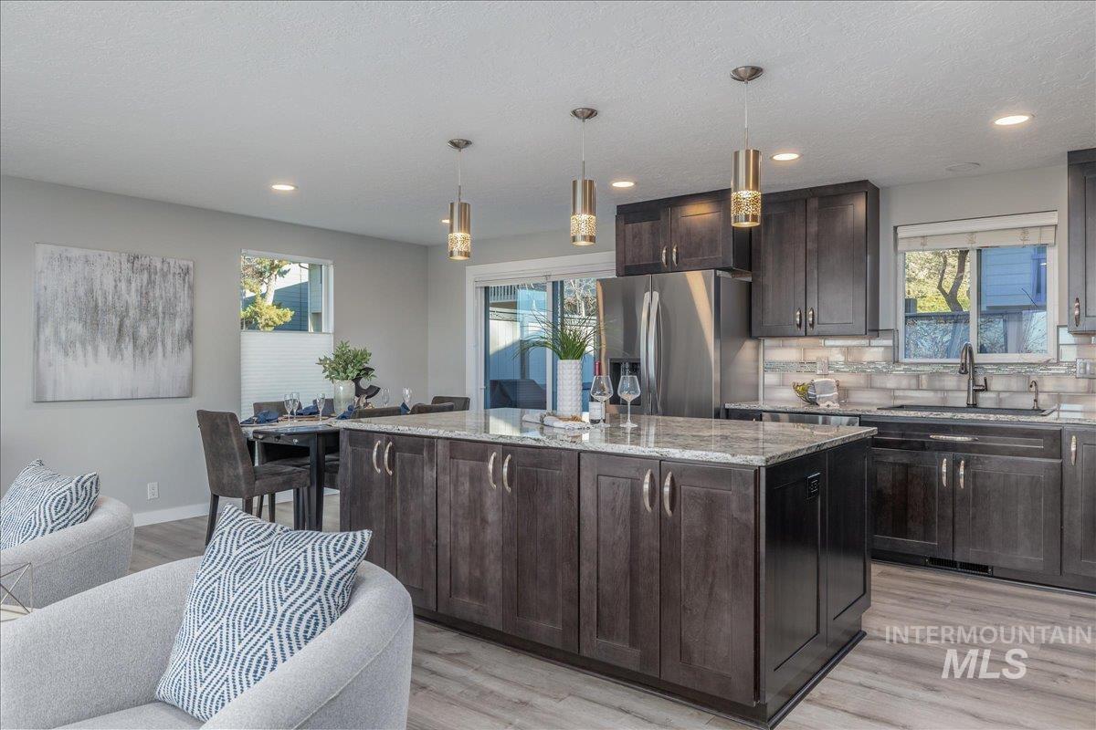 Kitchen with light stone countertops, a center island, stainless steel fridge, pendant lighting, and tasteful backsplash
