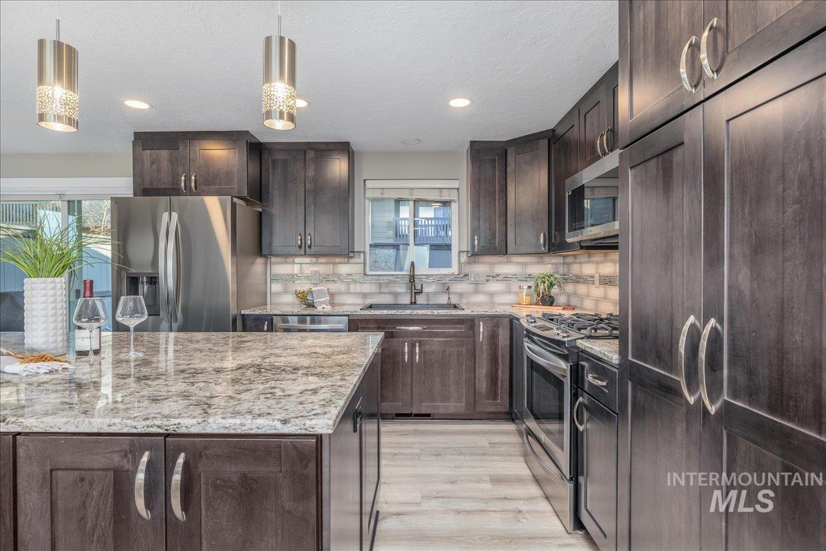 Kitchen with dark brown cabinetry, appliances with stainless steel finishes, light wood-style floors, light stone countertops, and recessed lighting