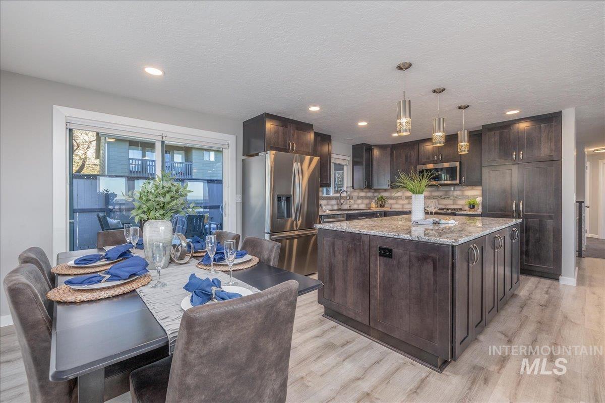 Kitchen with dark brown cabinetry, stainless steel appliances, light stone countertops, light wood-style flooring, and a center island