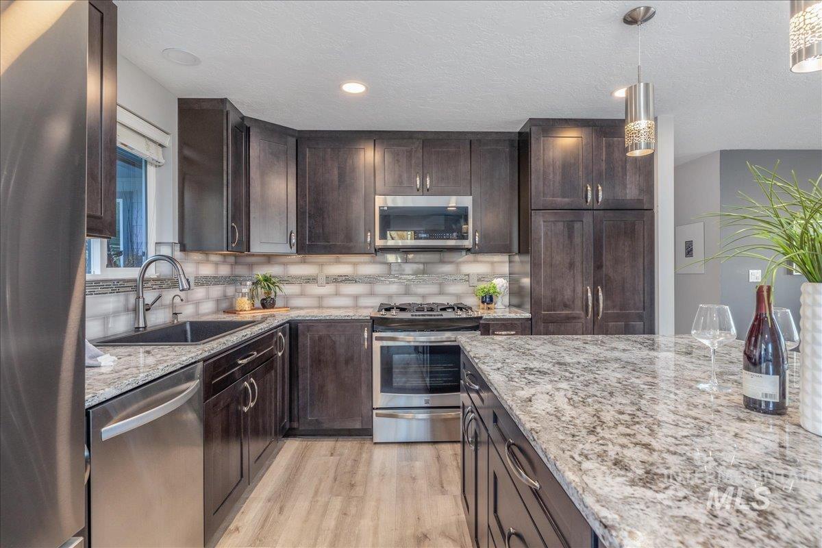 Kitchen featuring dark brown cabinetry, stainless steel appliances, light stone countertops, pendant lighting, and a textured ceiling