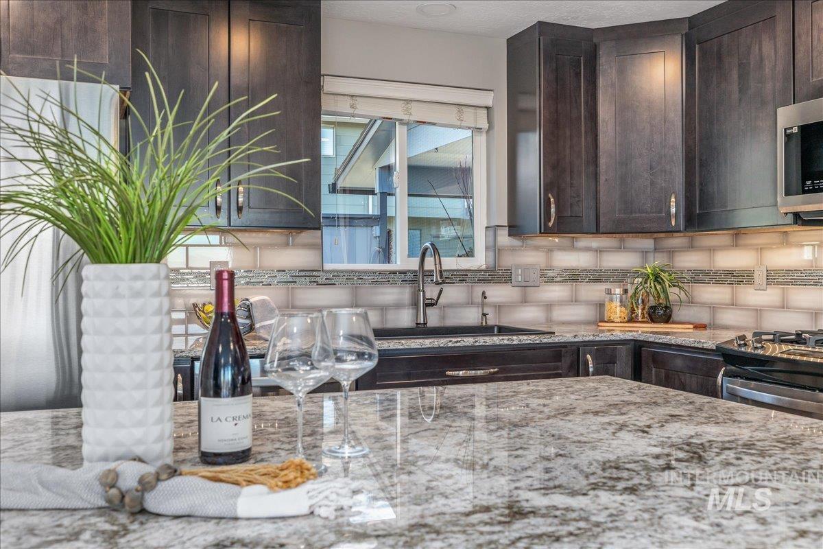 Kitchen featuring dark brown cabinetry, light stone counters, tasteful backsplash, and appliances with stainless steel finishes