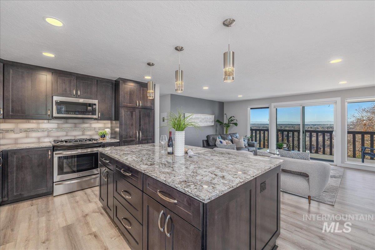 Kitchen featuring dark brown cabinetry, stainless steel appliances, decorative light fixtures, light stone countertops, and recessed lighting