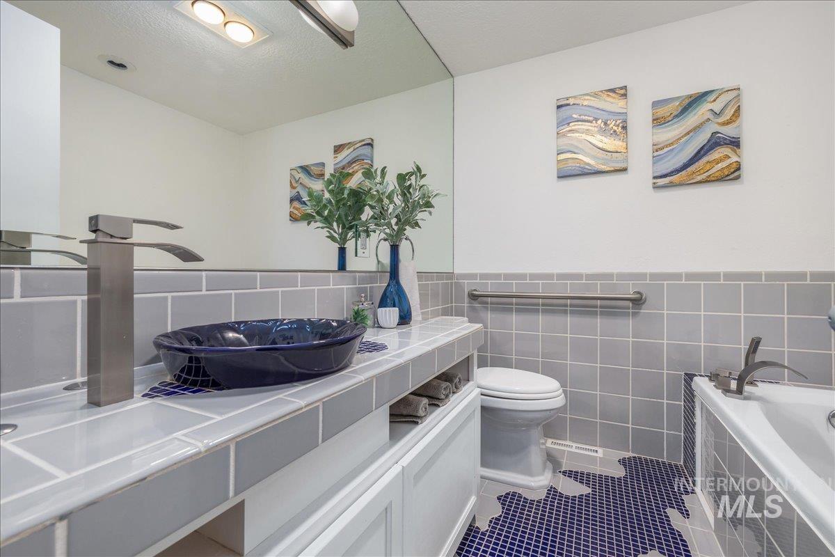 Full bath featuring tile patterned floors, tiled bath, vanity, tile walls, and wainscoting