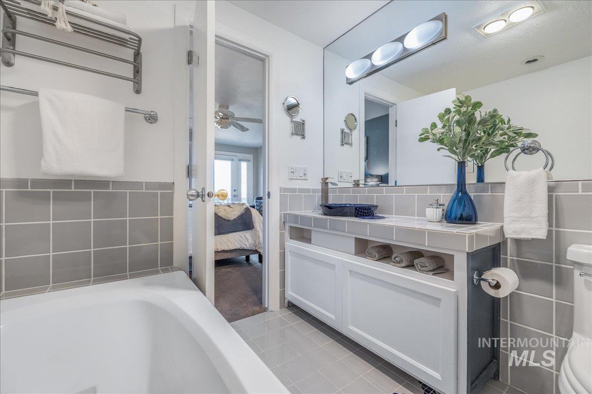 Ensuite bathroom with vanity, a bathtub, light tile patterned floors, ceiling fan, and tile walls