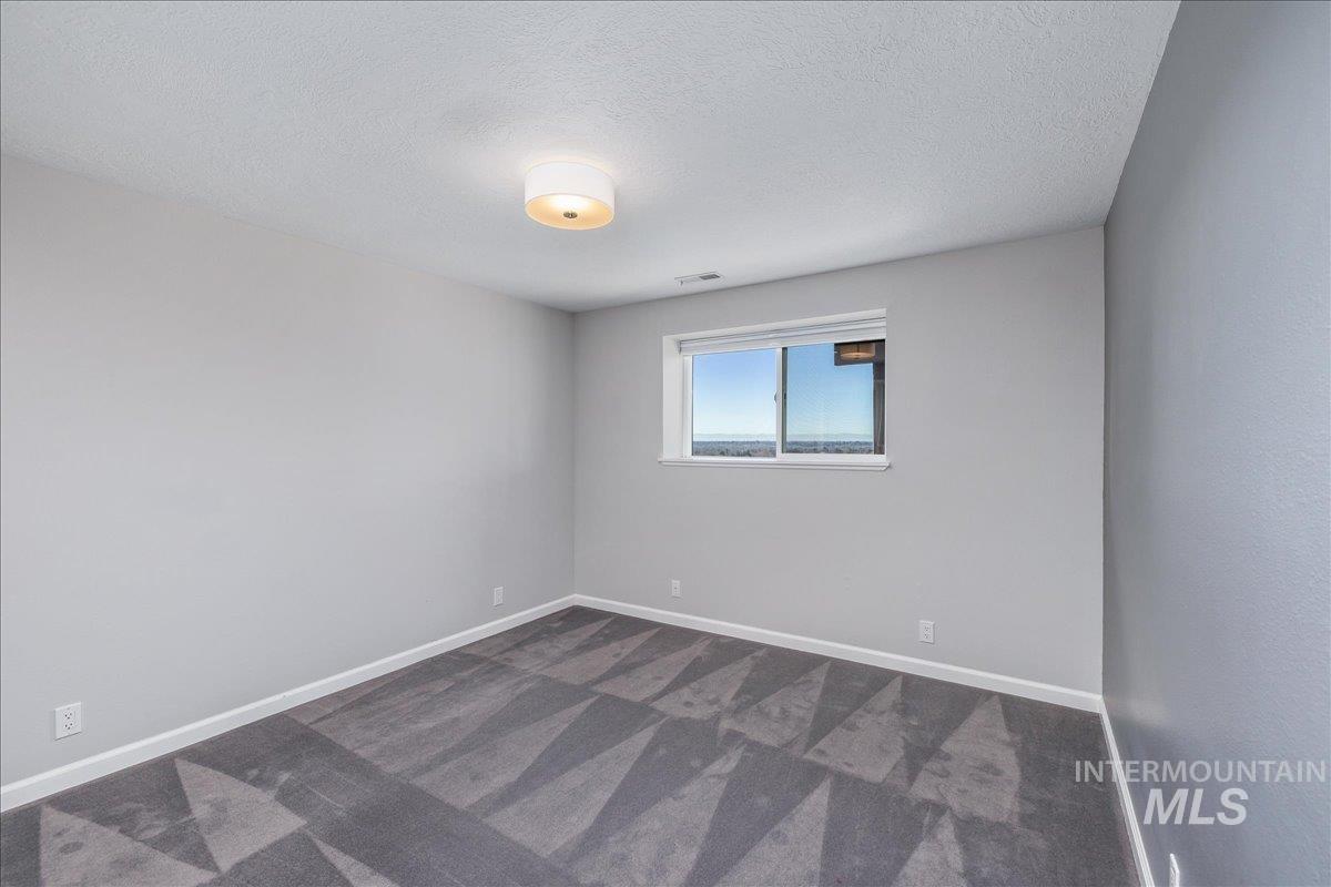 Empty room featuring dark carpet and a textured ceiling