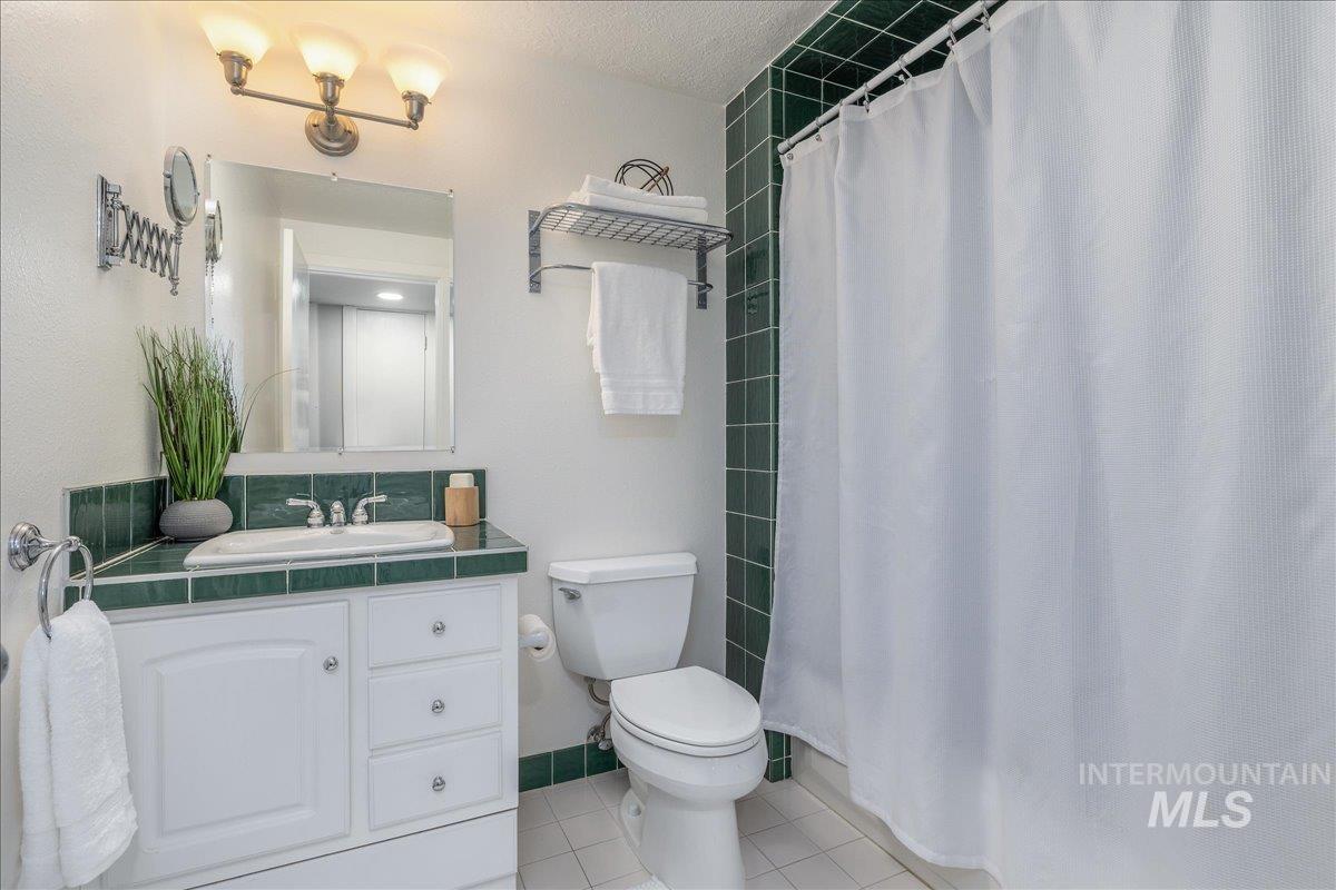 Full bathroom featuring a shower with shower curtain, vanity, light tile patterned floors, and a textured ceiling
