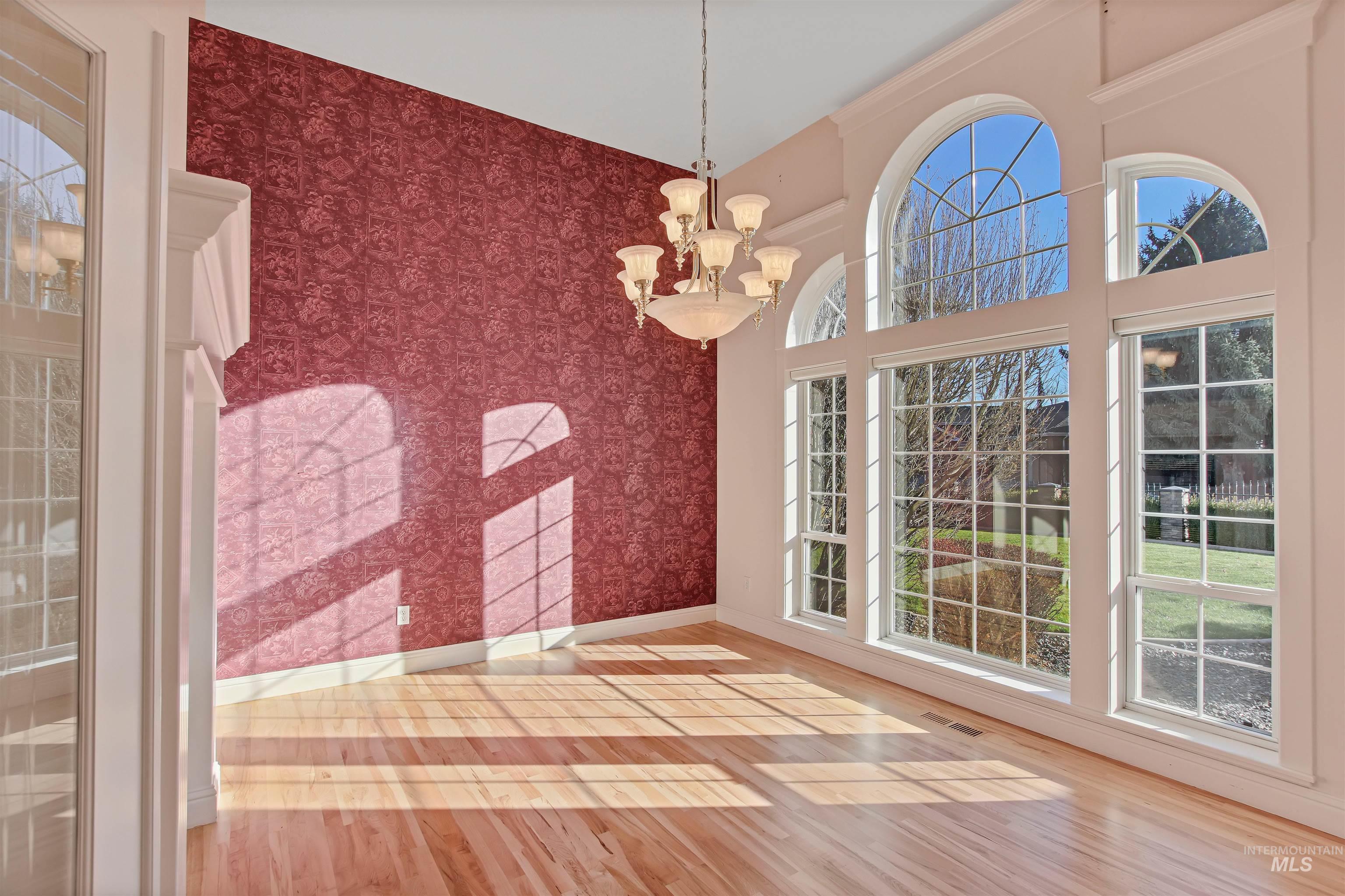 Unfurnished dining area with a chandelier, wood finished floors, an accent wall, wallpapered walls, and a high ceiling