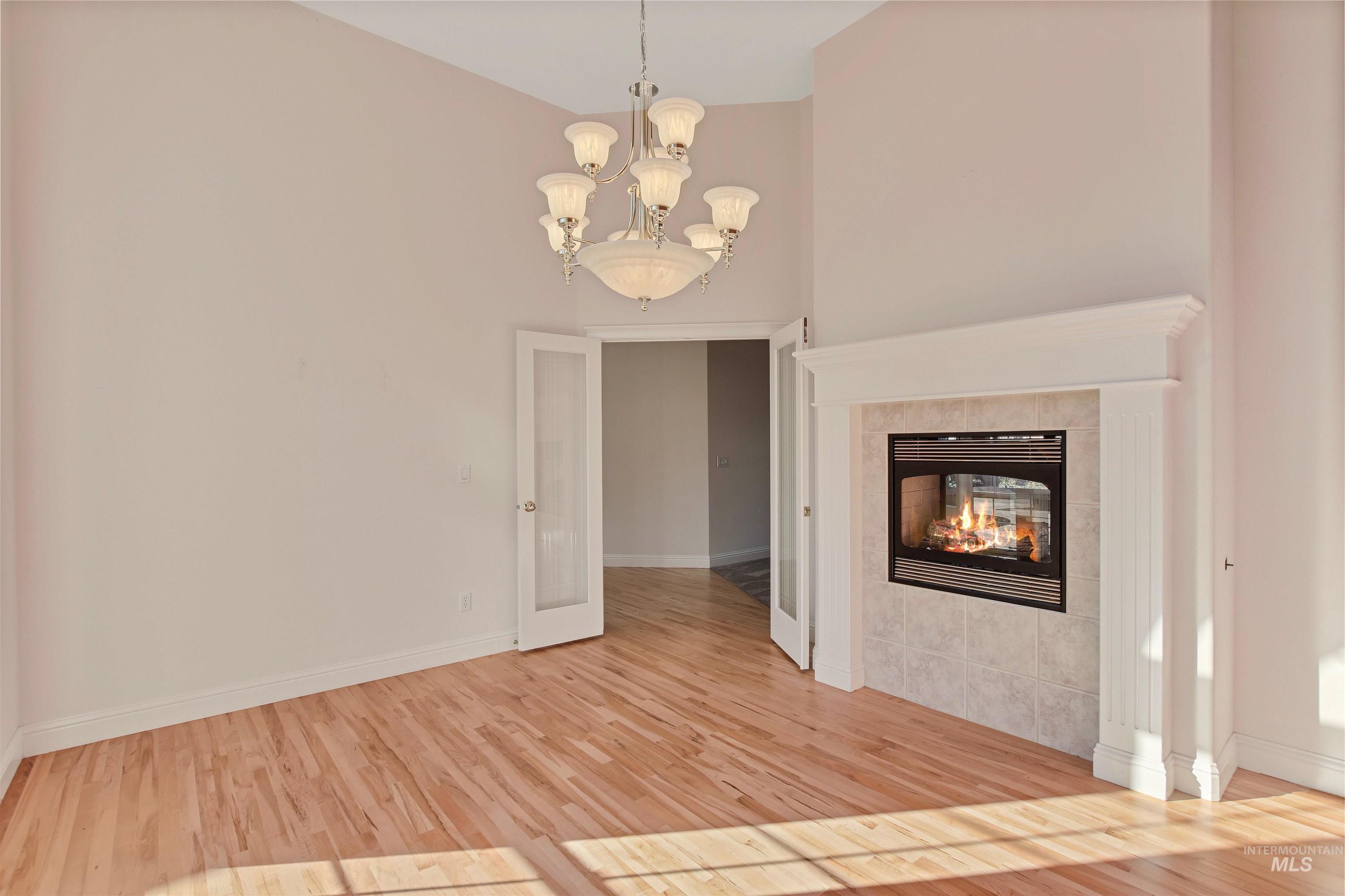 Unfurnished living room featuring a tile fireplace, light wood-style floors, and a chandelier