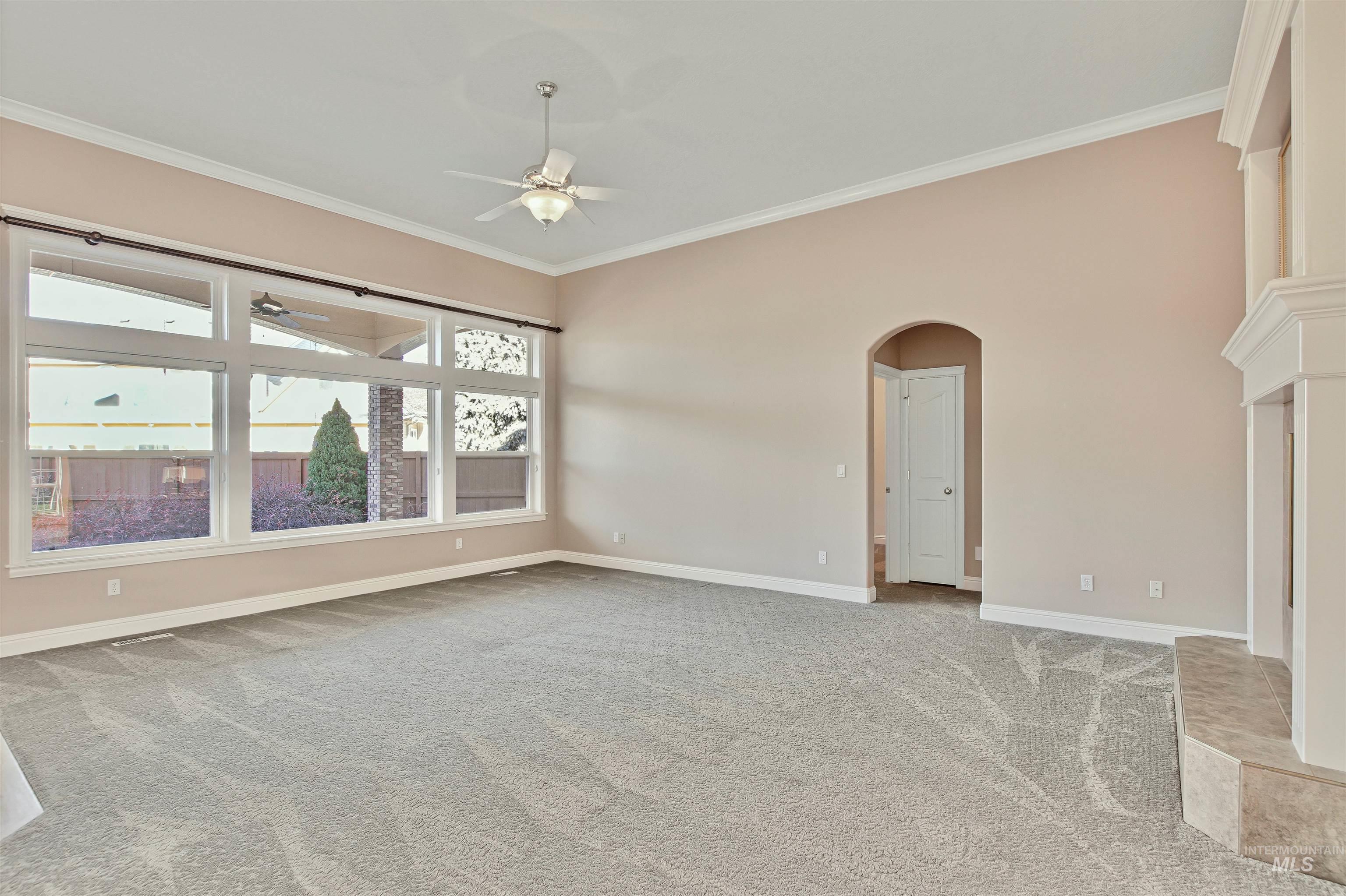 Unfurnished room with ornamental molding, arched walkways, light carpet, and a ceiling fan