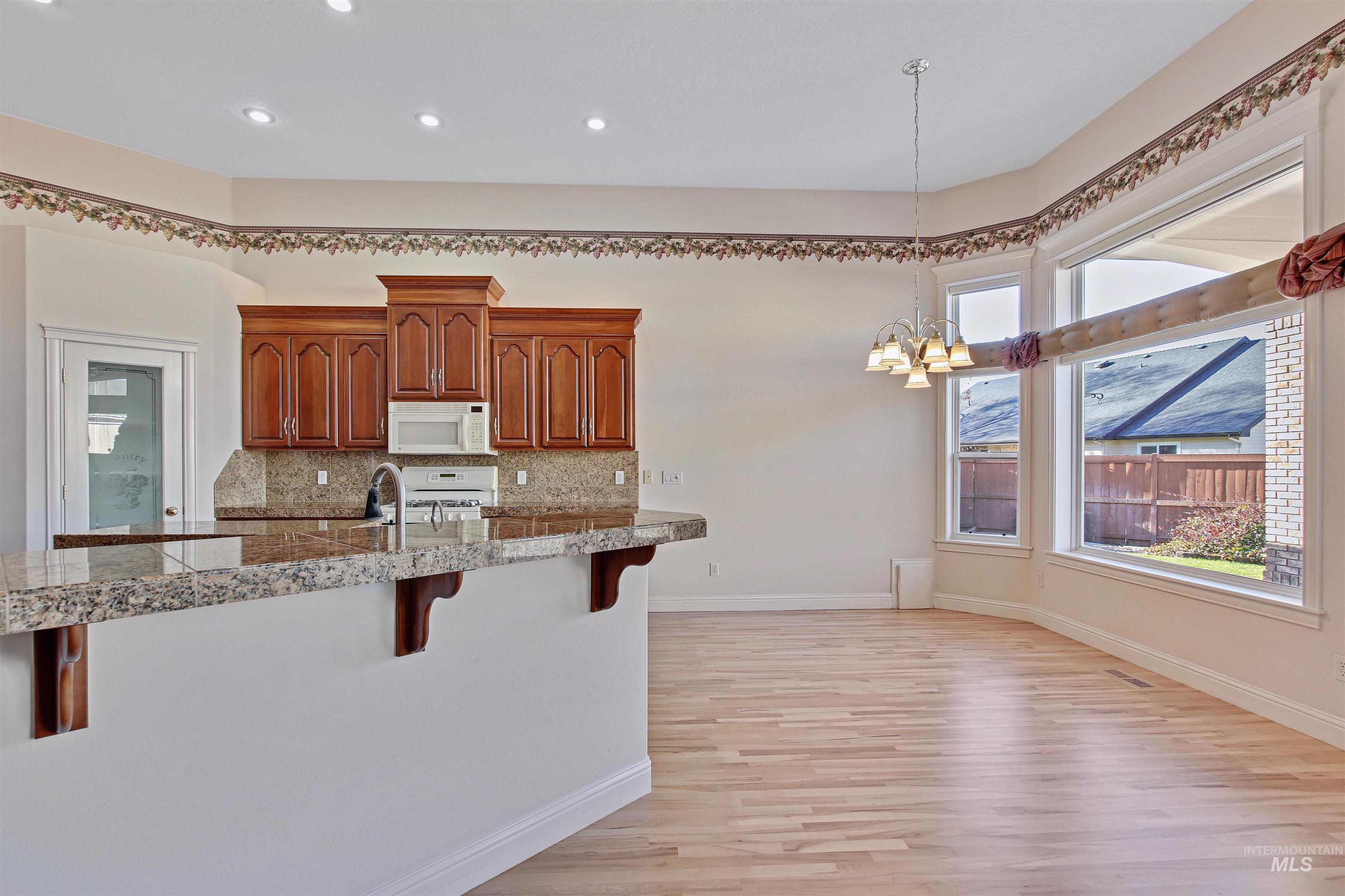 Kitchen featuring a breakfast bar, hanging light fixtures, brown cabinetry, decorative backsplash, and tile counters