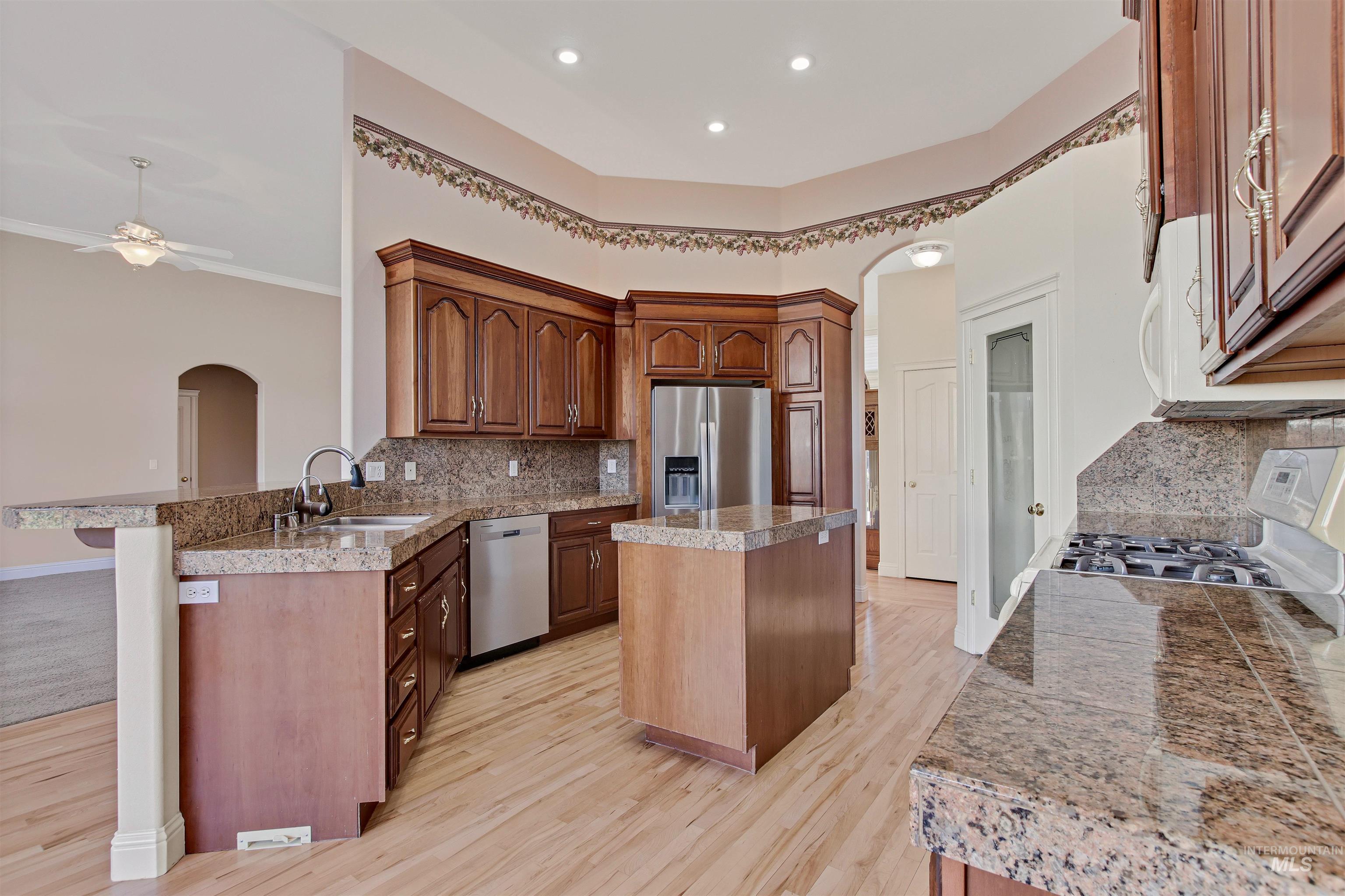 Kitchen featuring tile counters, arched walkways, a kitchen island, decorative backsplash, and a peninsula