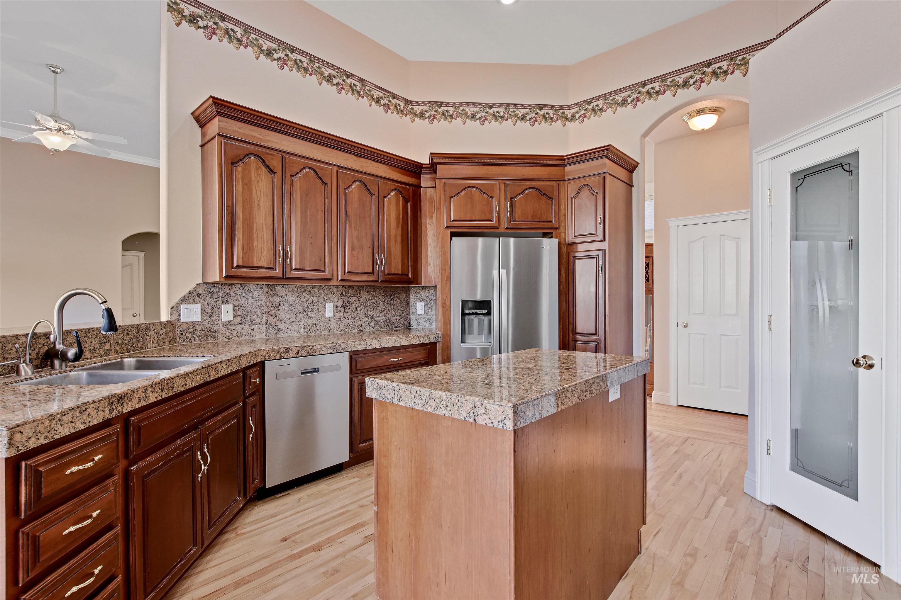 Kitchen with arched walkways, tile counters, appliances with stainless steel finishes, a kitchen island, and backsplash