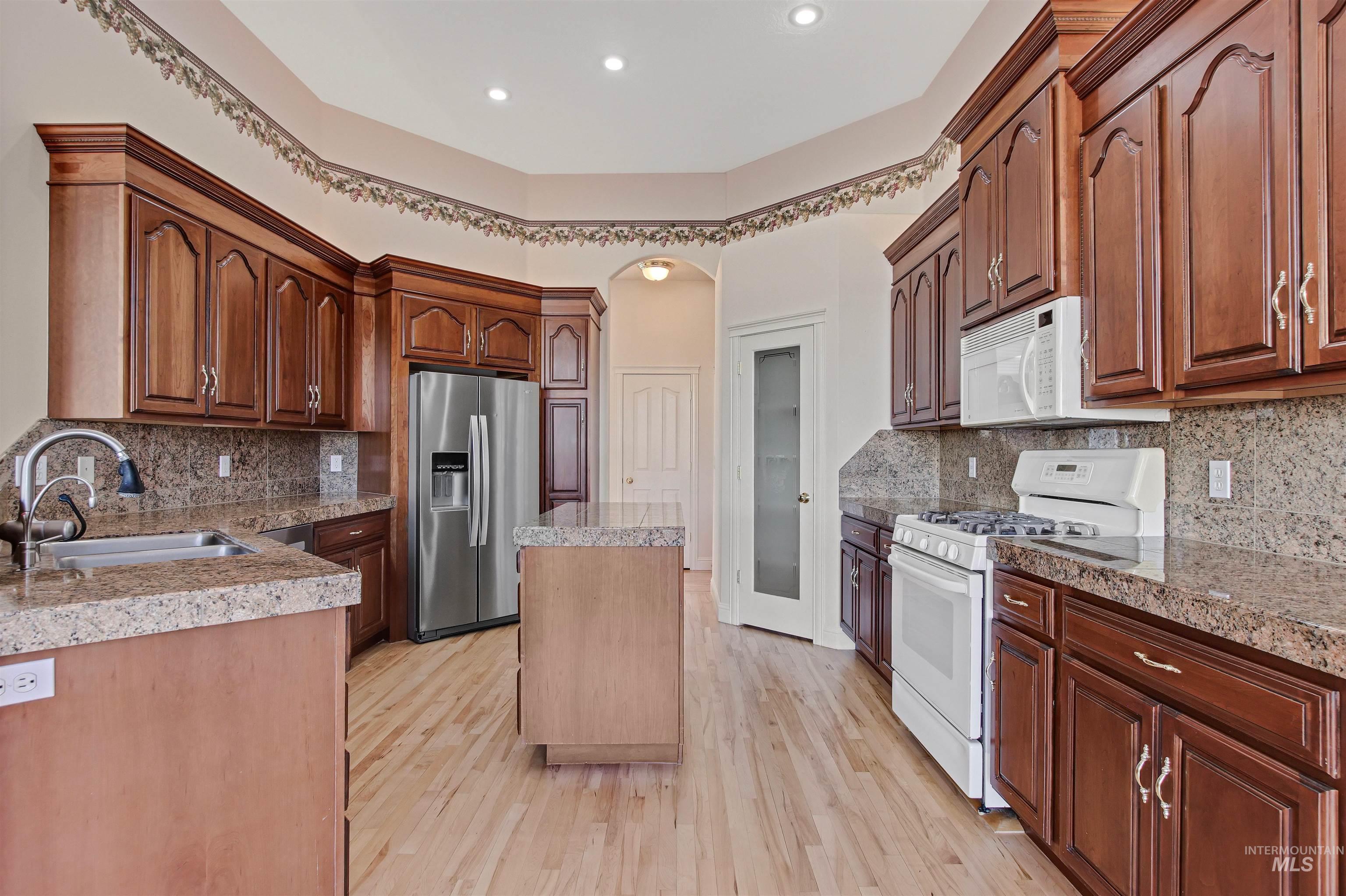 Kitchen featuring tile countertops, white appliances, light wood finished floors, and backsplash
