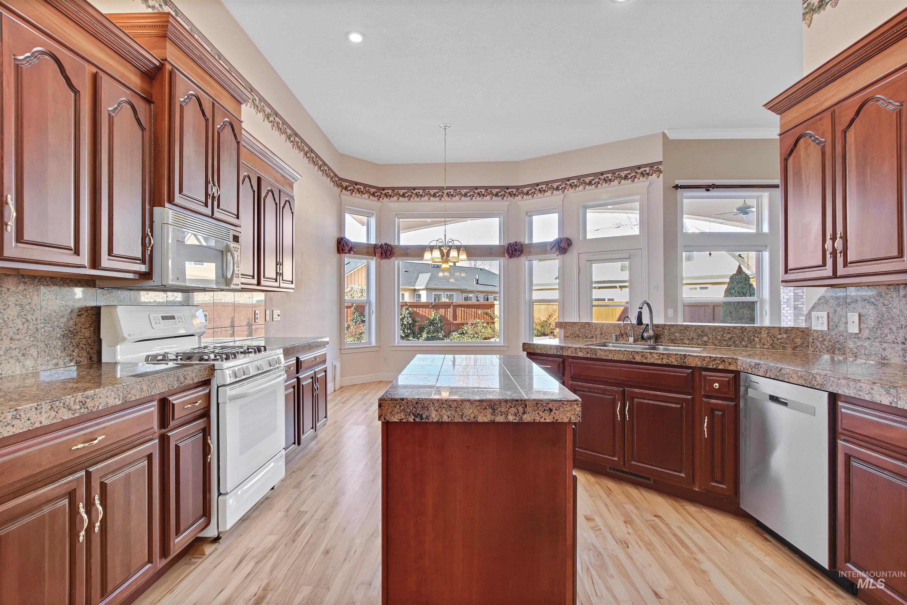 Kitchen featuring tasteful backsplash, tile countertops, white appliances, a chandelier, and a kitchen island
