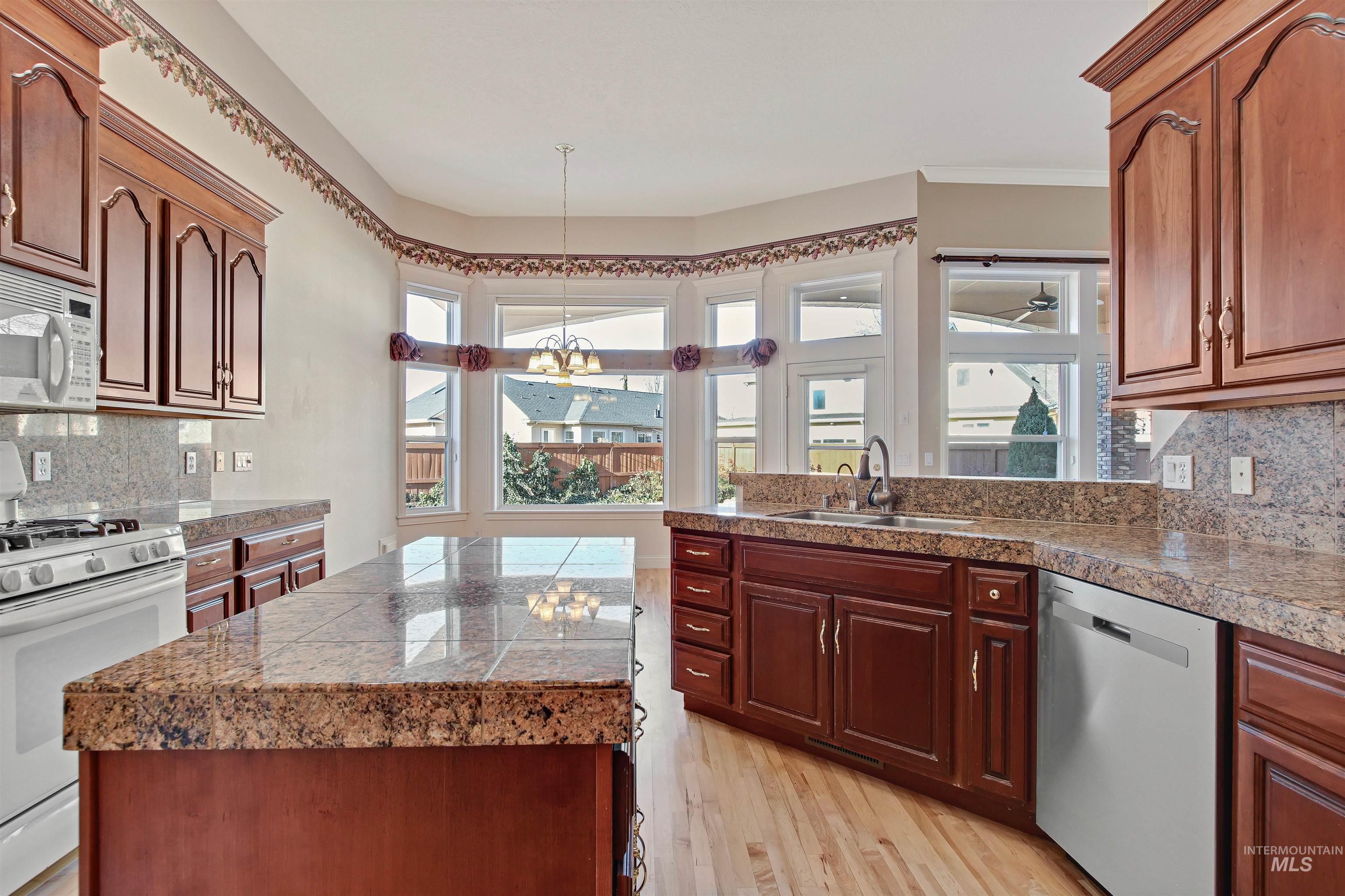 Kitchen with tasteful backsplash, tile counters, white appliances, and hanging light fixtures