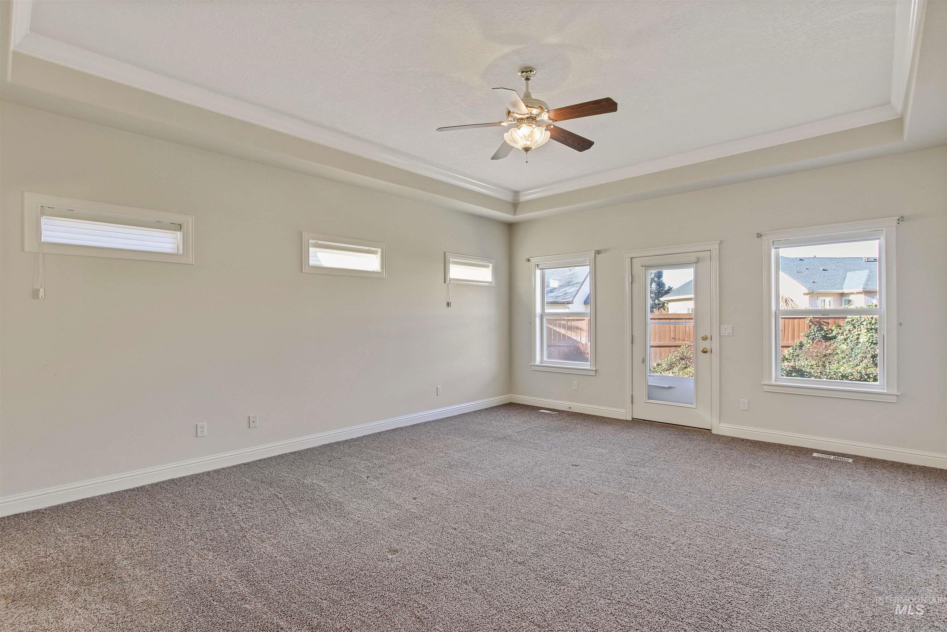 Empty room featuring a tray ceiling, light carpet, healthy amount of natural light, a ceiling fan, and crown molding