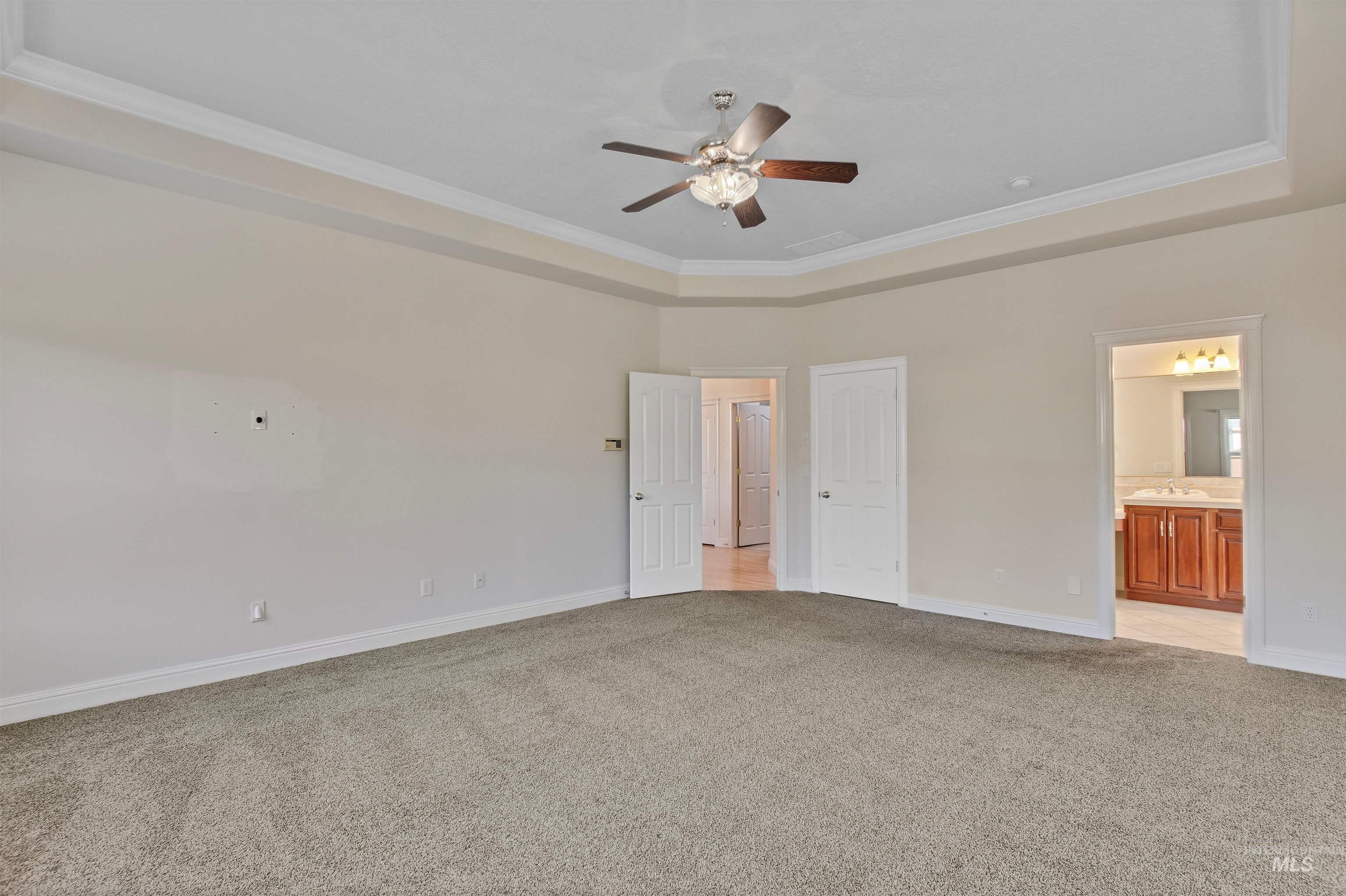 Unfurnished bedroom featuring crown molding, a raised ceiling, light colored carpet, ensuite bathroom, and a ceiling fan