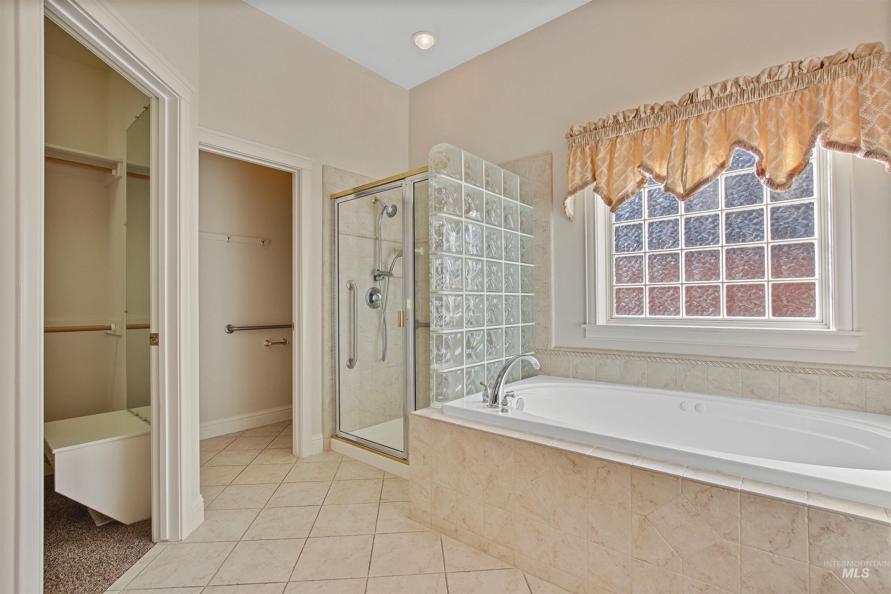Full bathroom with a garden tub, a spacious closet, a shower stall, and light tile patterned floors