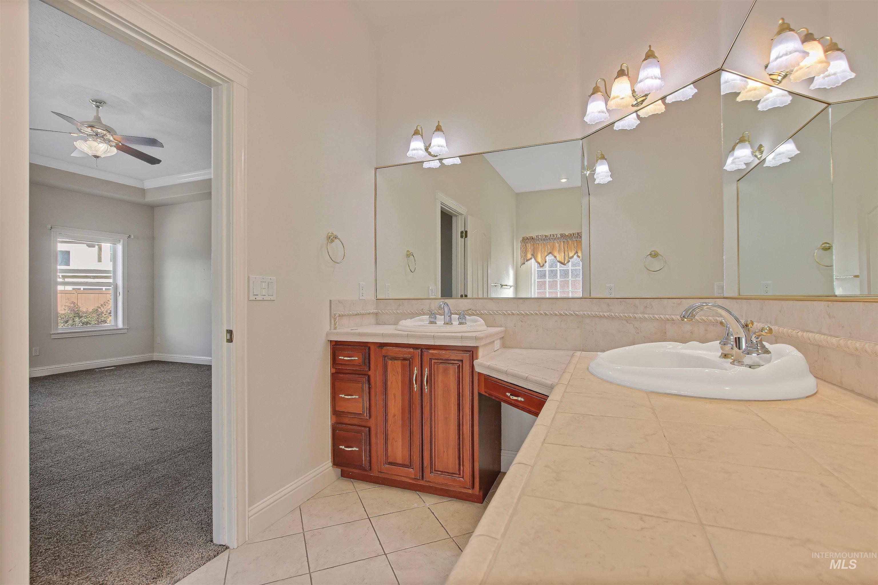 Bathroom featuring double vanity, light tile patterned flooring, light carpet, and a ceiling fan
