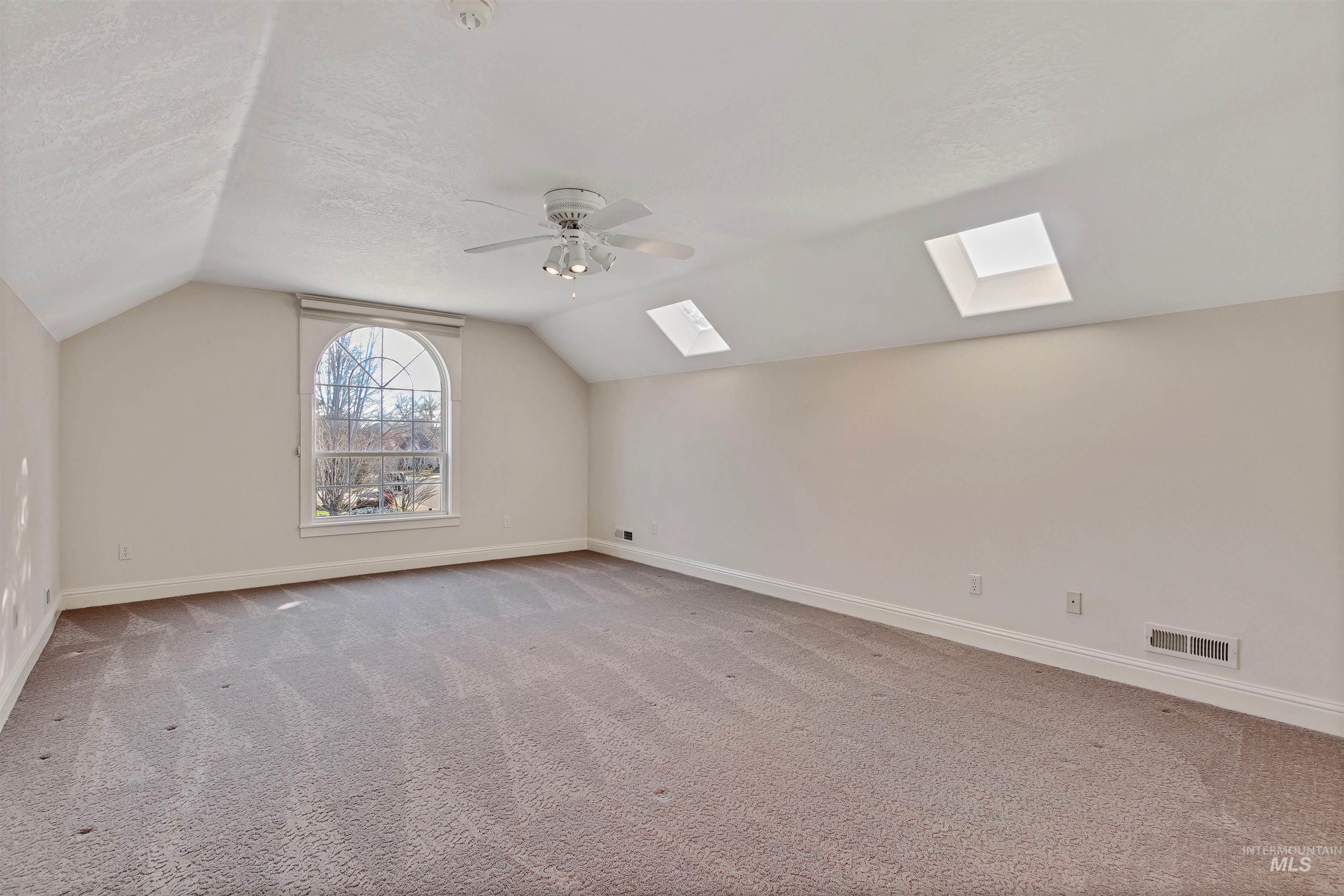 Additional living space with light colored carpet, a skylight, vaulted ceiling, ceiling fan, and a textured ceiling